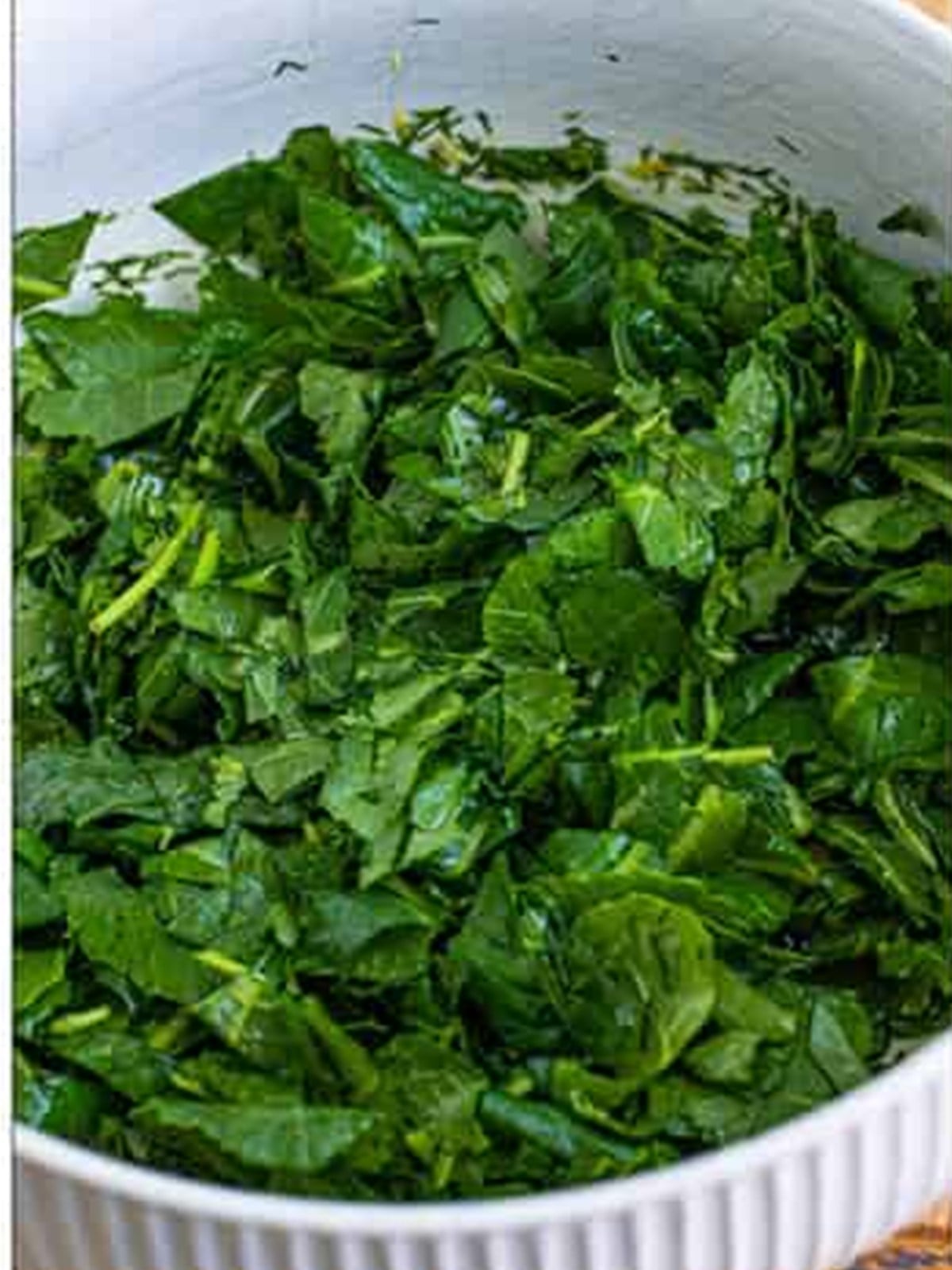 Chopped baby kale tossed with the dressing in a bowl.