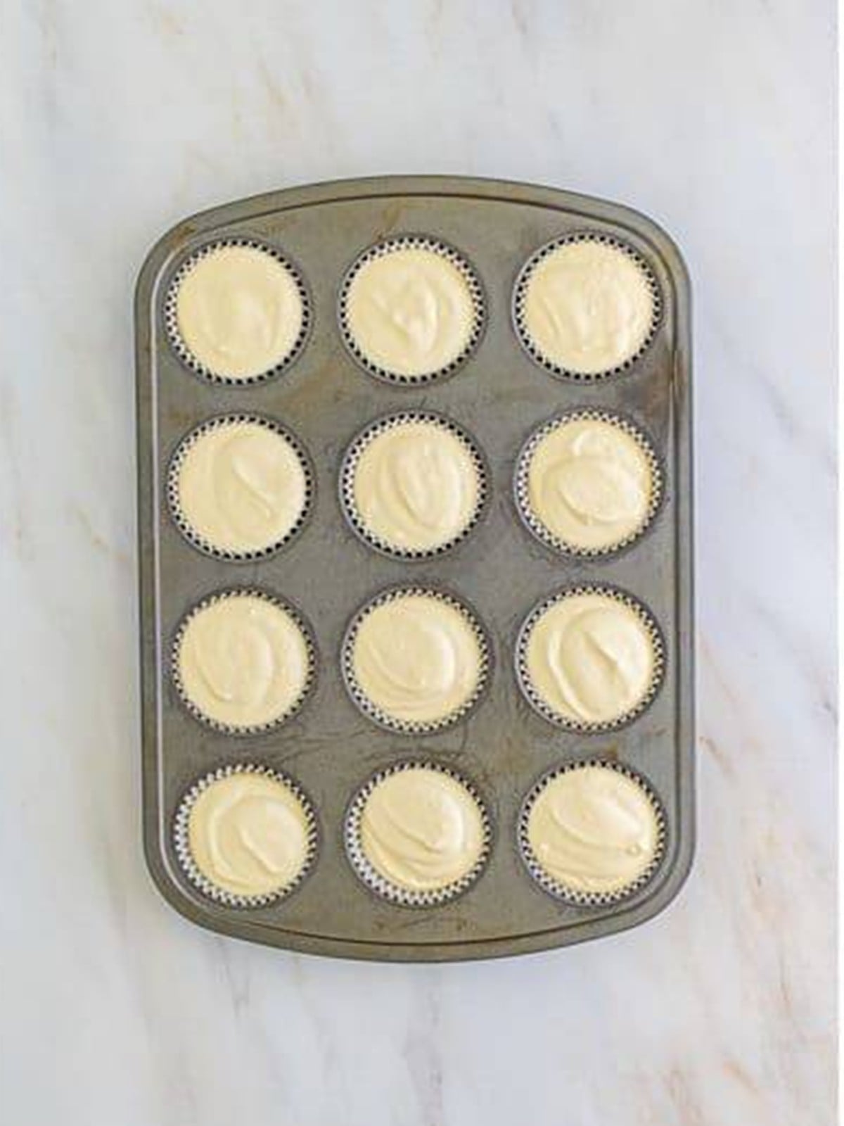 Key lime cheesecake filling spooned into the lined muffin tin over the crusts.