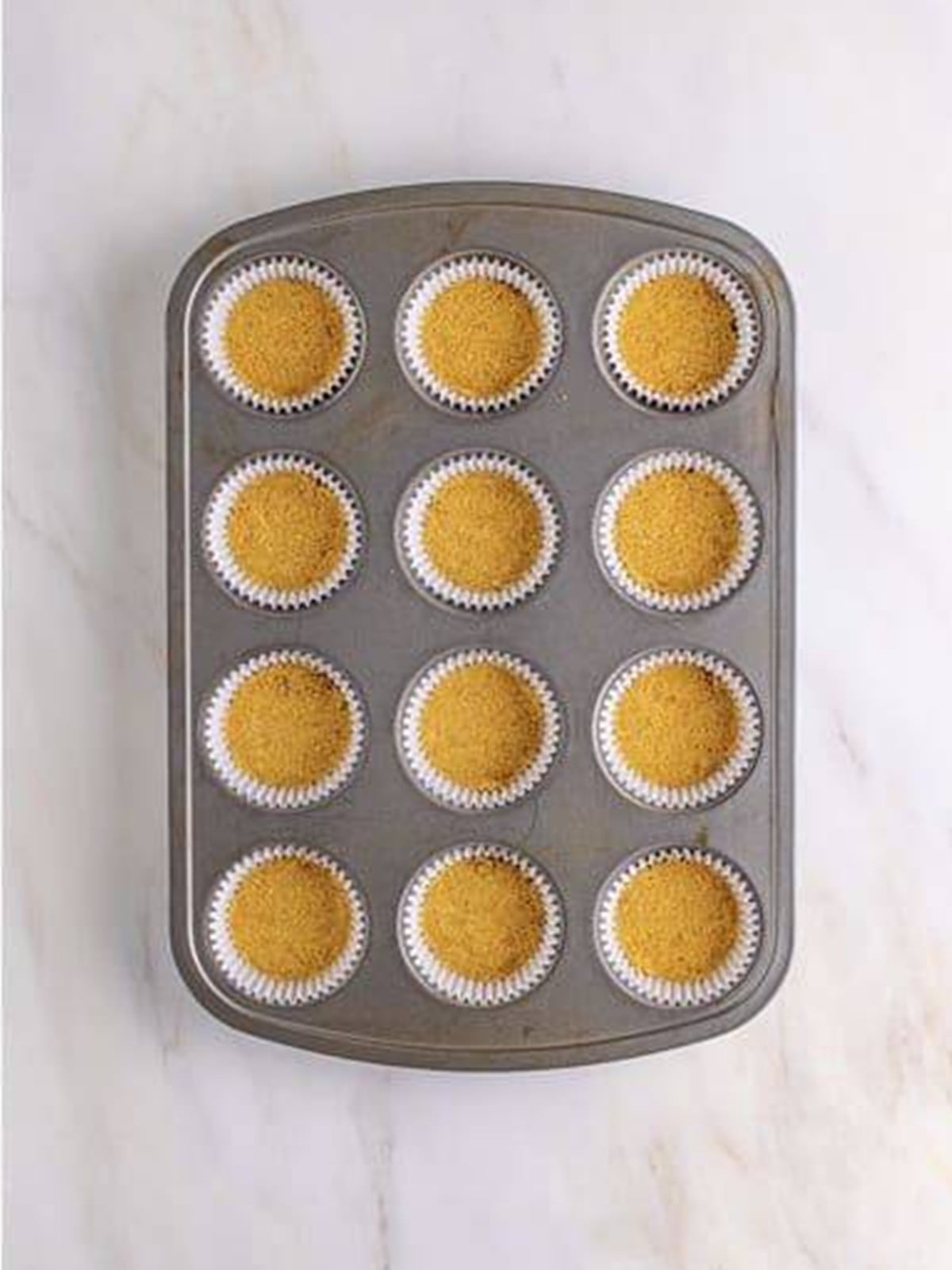 Graham cracker crust pressed into a lined muffin tin for mini Key Lime Cheesecakes.