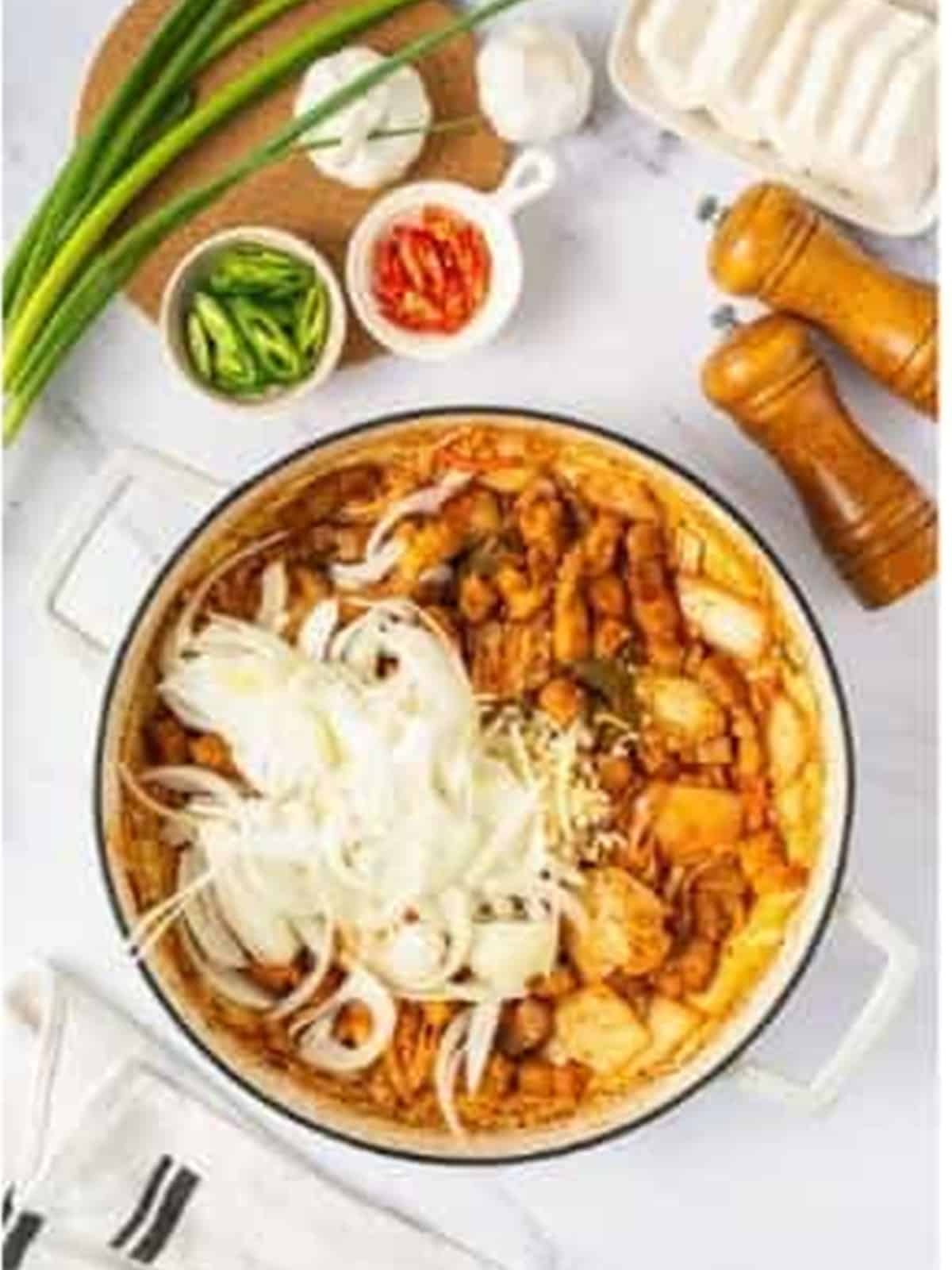 Sliced onion and minced garlic added to the pork belly and kimchi in the pot.