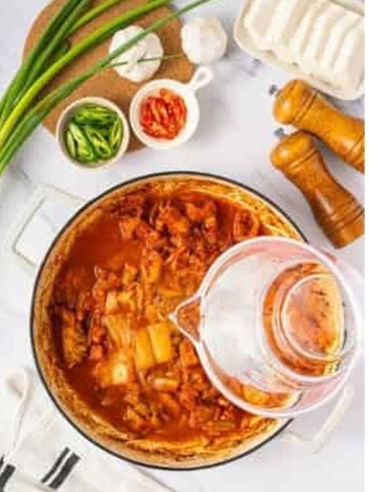 Water being poured into the pot of kimchi and pork to make the stew.