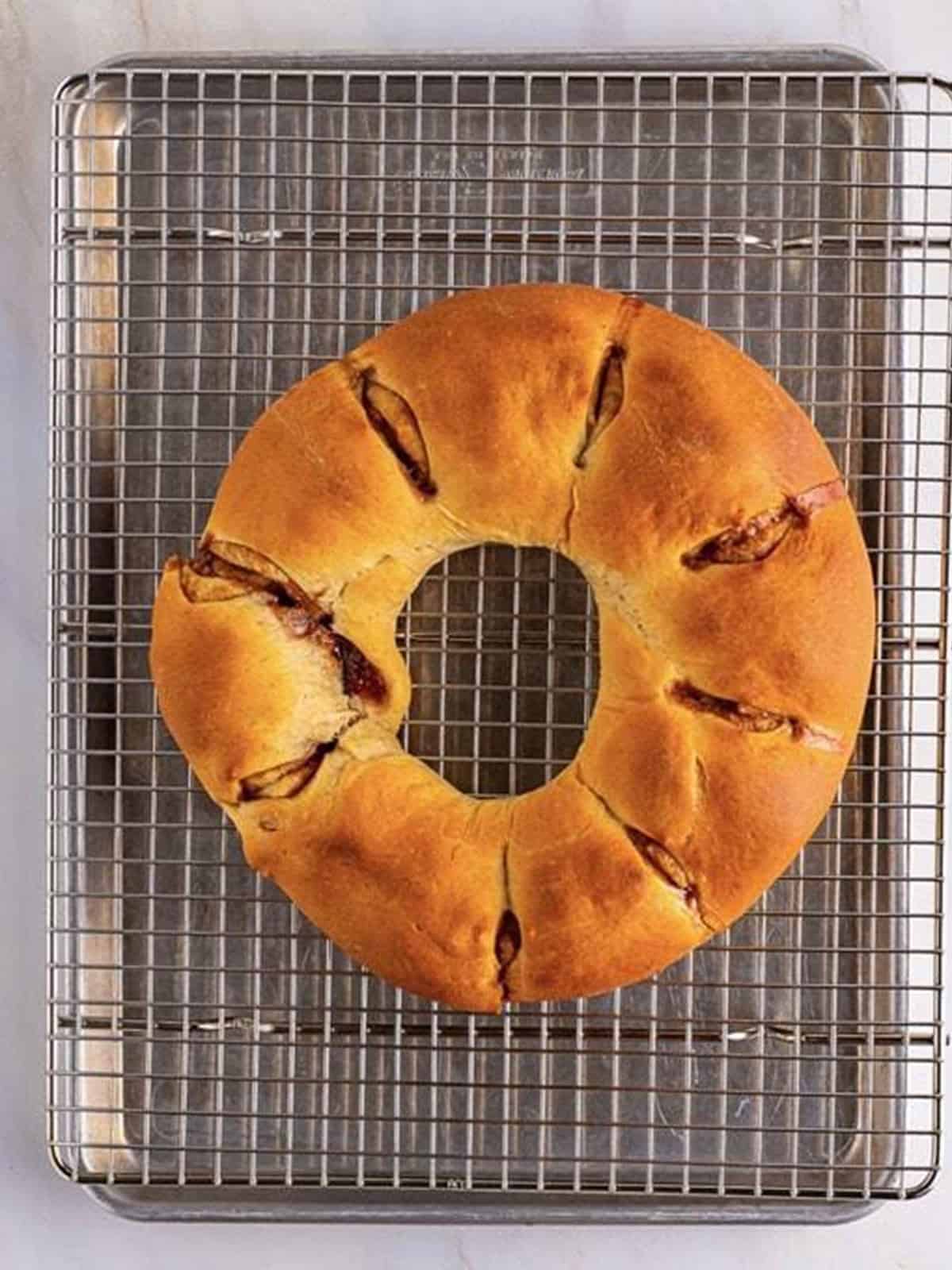 A golden-brown baked king cake ring cooling on a wire rack.