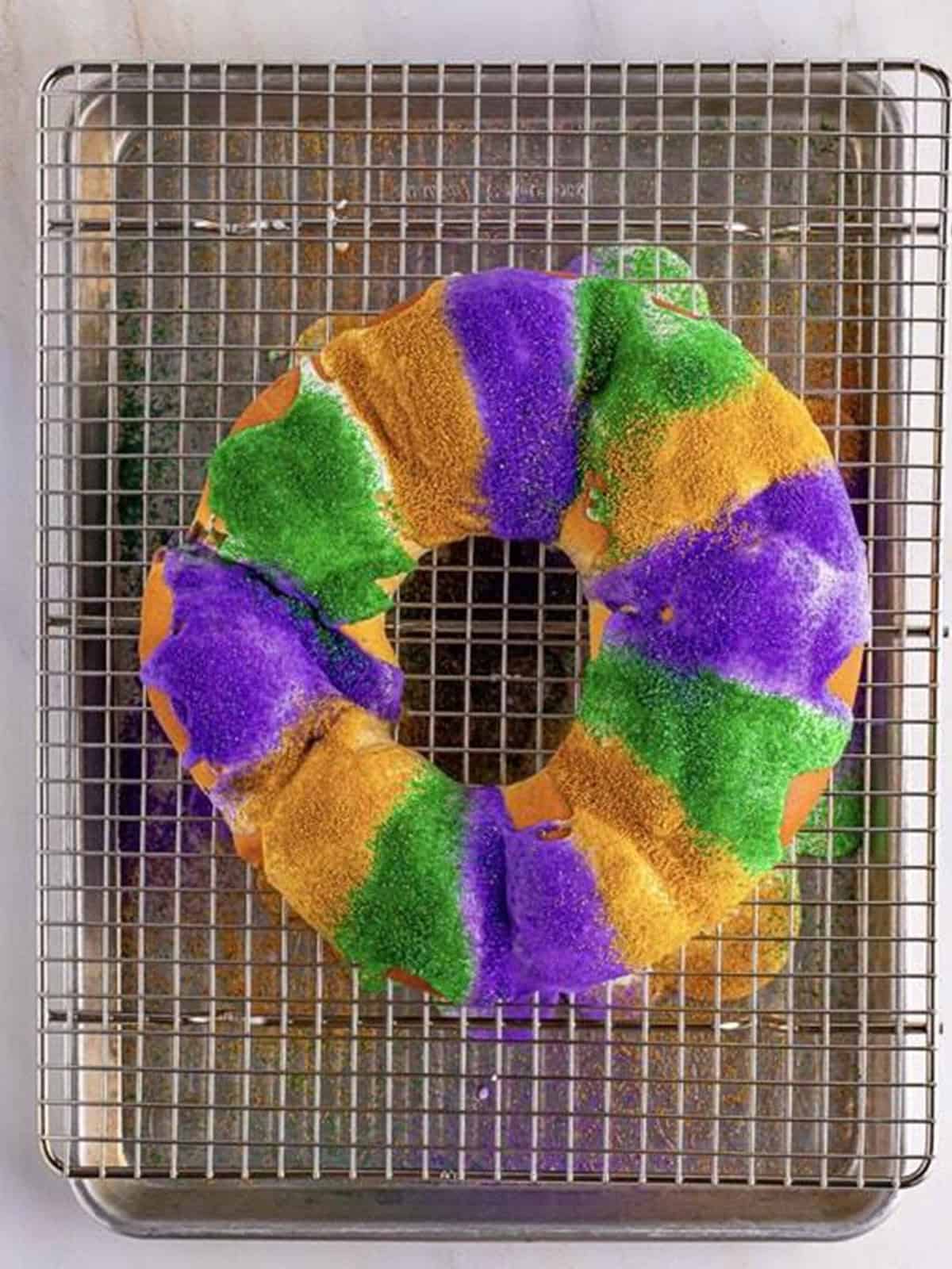 The king cake glazed and decorated with bands of purple, green, and gold sanding sugar.