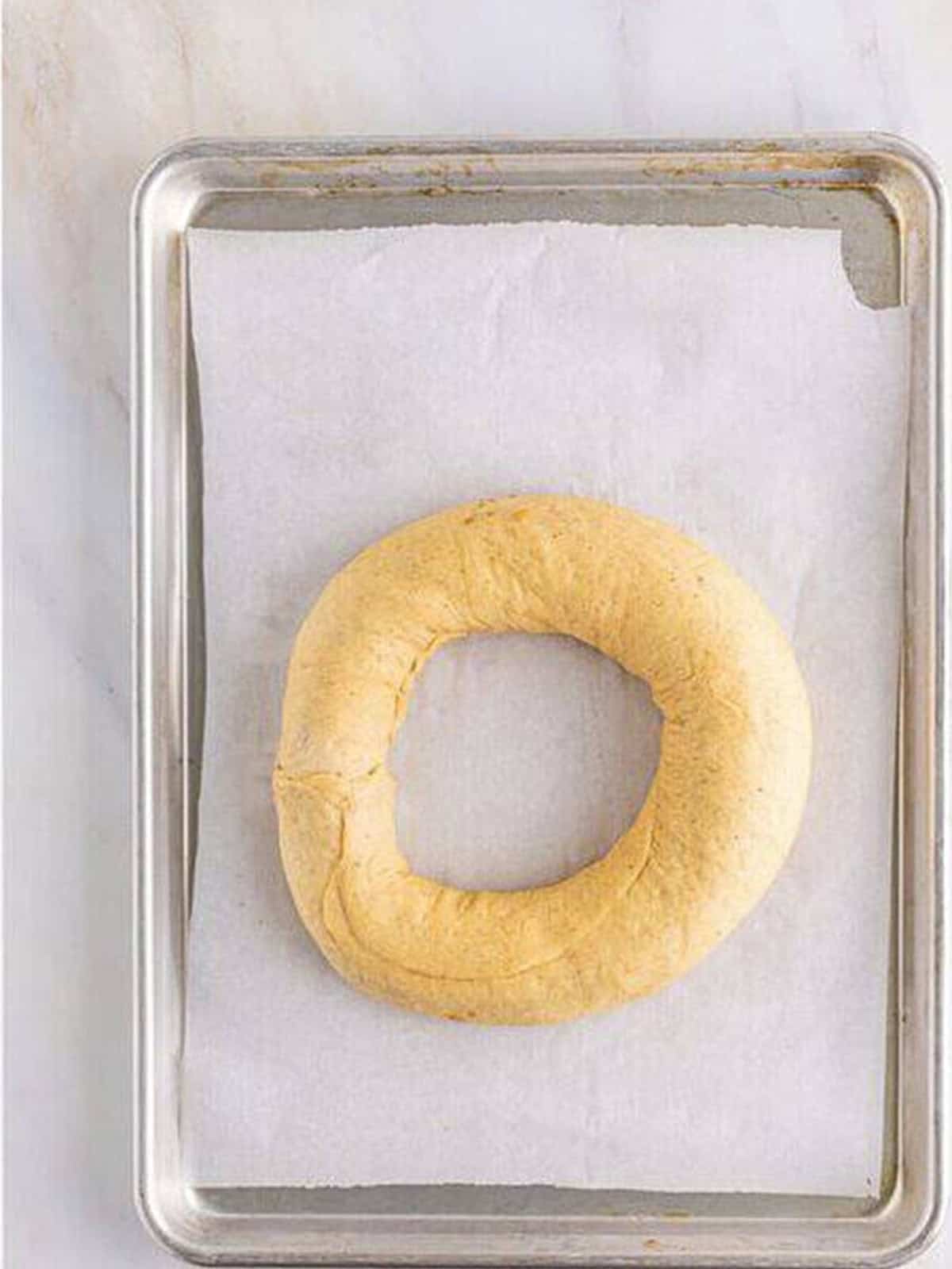 The king cake dough log shaped into a ring on a parchment-lined baking sheet.