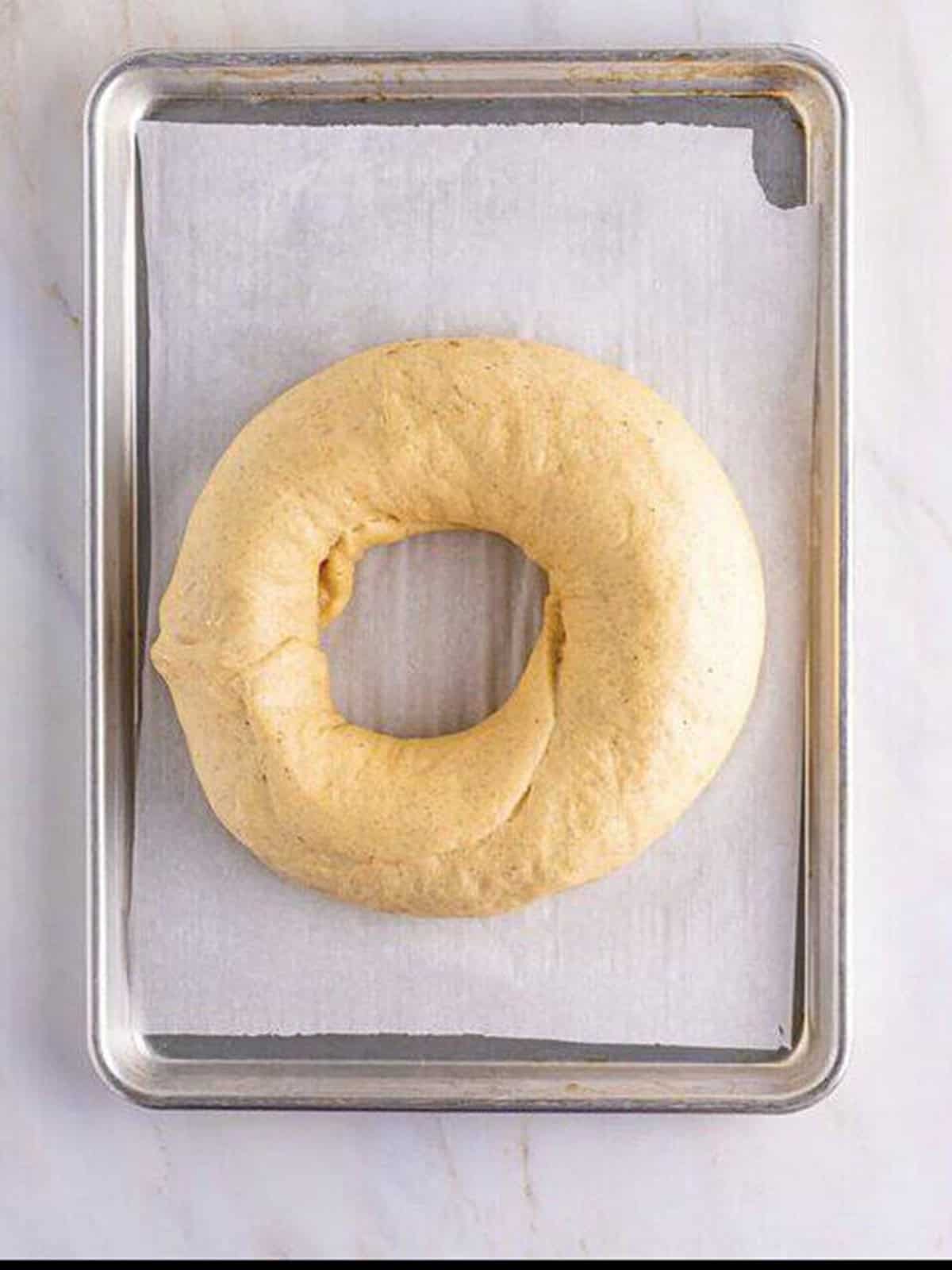 The shaped king cake ring rising on a baking sheet before baking.