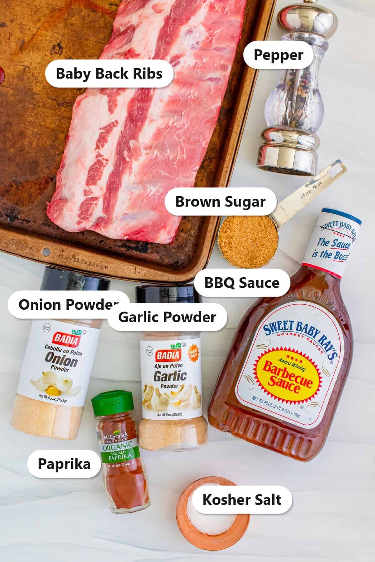 Labeled ingredients for slow cooker ribs including baby back ribs, brown sugar, smoked paprika, garlic powder, onion powder, kosher salt, pepper, and BBQ sauce.