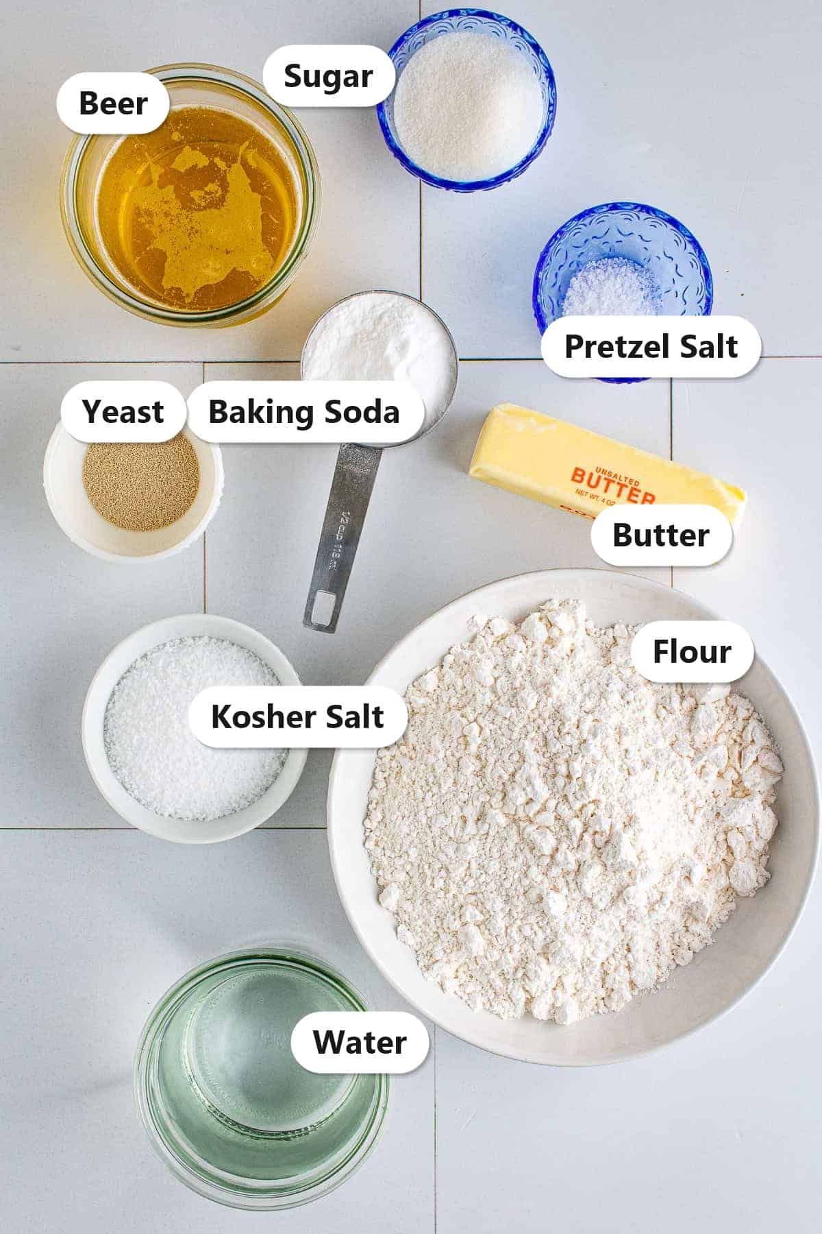 Labeled ingredients for homemade soft pretzels including flour, beer, yeast, sugar, kosher salt, baking soda, butter, and pretzel salt.