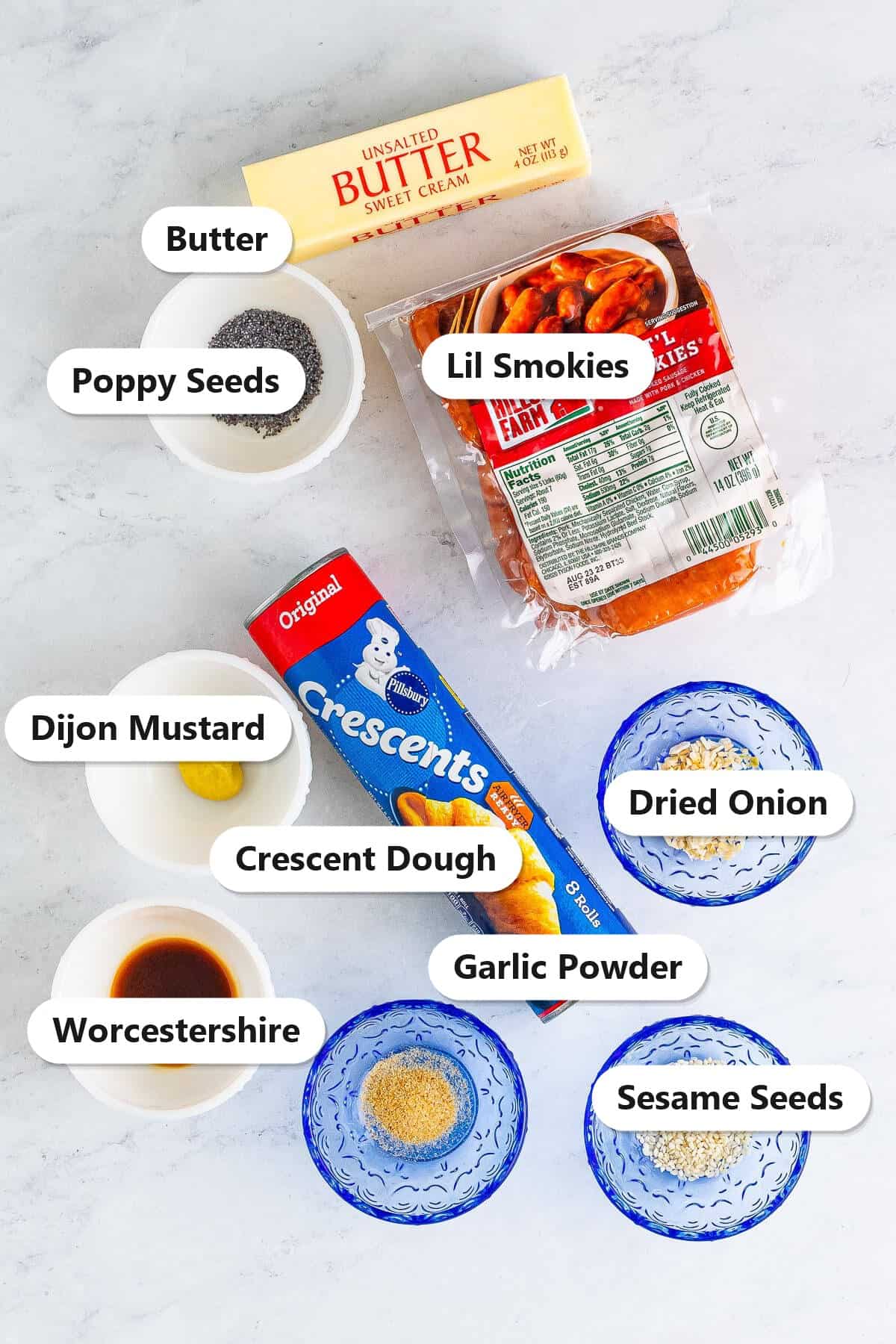 Labeled ingredients to make pigs in a blanket including lil smokies, crescent dough, butter, poppy seeds, sesame seeds, and seasonings.