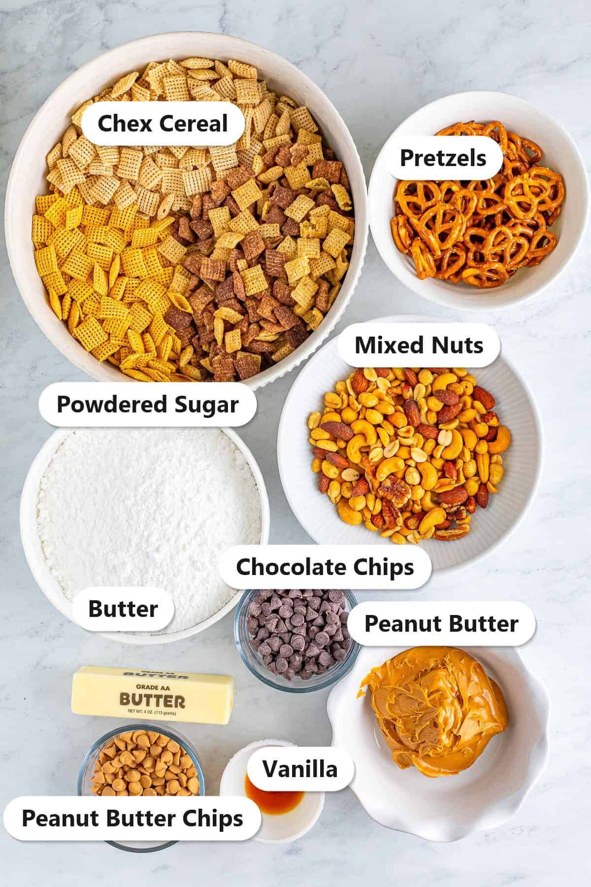 Labeled ingredients for puppy chow including Chex cereal, chocolate chips, peanut butter, butter, powdered sugar, vanilla, peanut butter chips, pretzels, and mixed nuts.