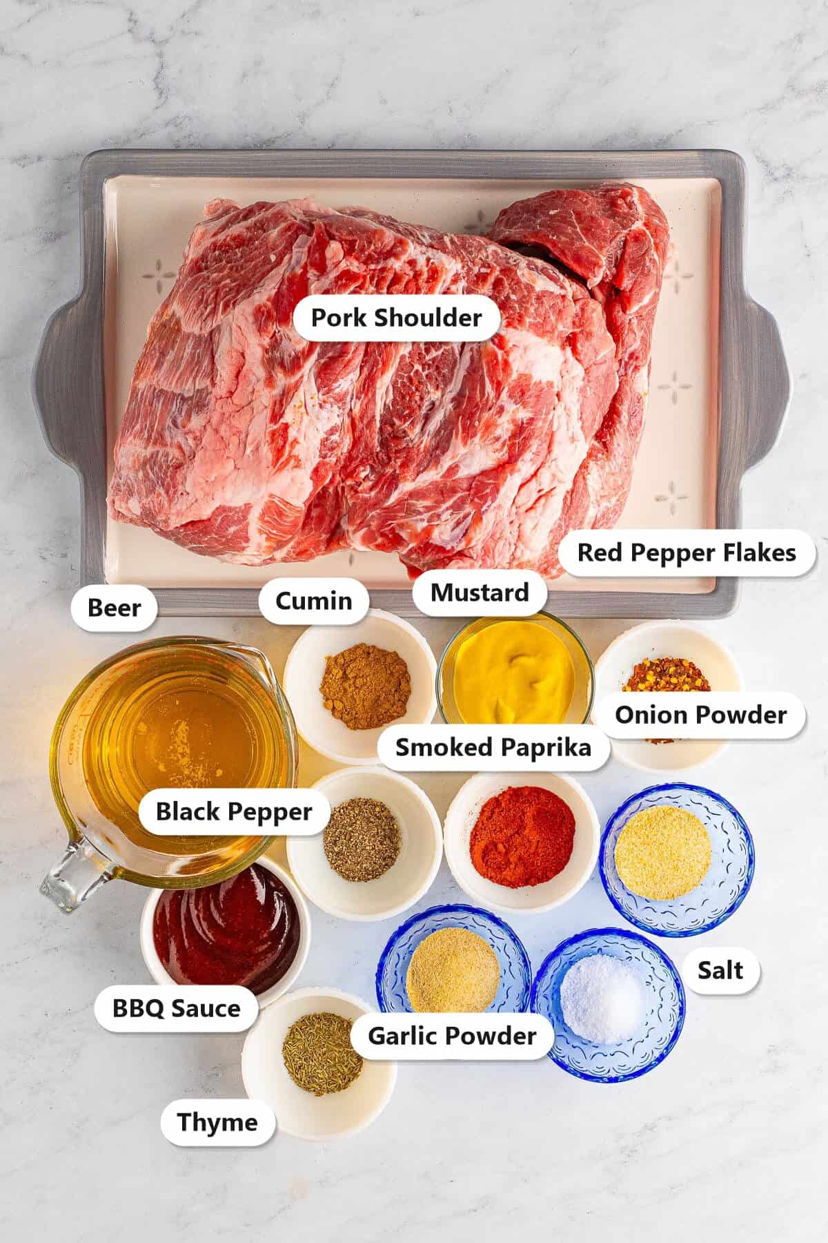 Labeled ingredients for oven baked pulled pork including pork shoulder, yellow mustard, smoked paprika, garlic powder, onion powder, cumin, thyme, beer, and BBQ sauce.