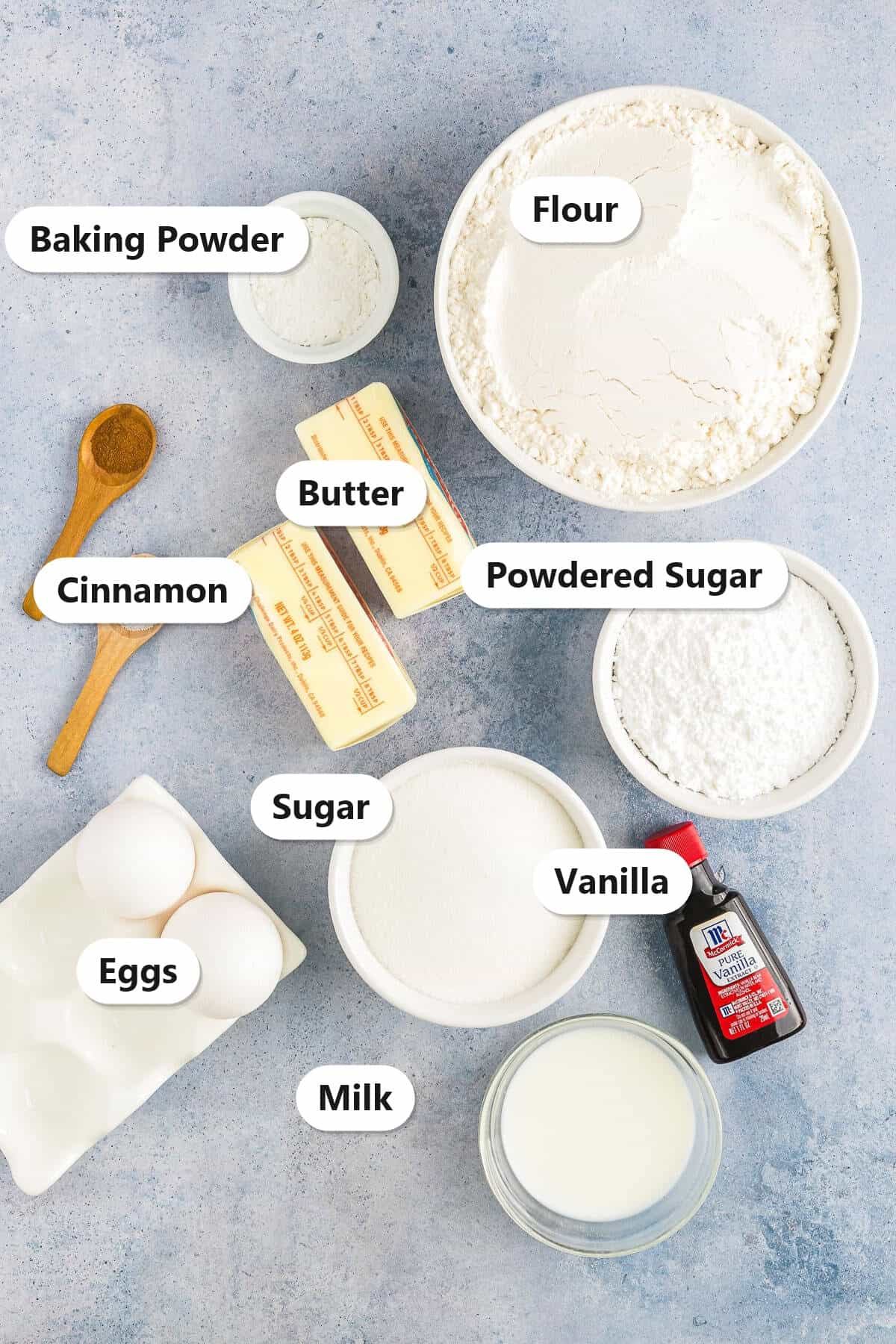 Labeled ingredients for cinnamon tea cakes including flour, butter, sugar, eggs, milk, baking powder, cinnamon, vanilla, and powdered sugar.