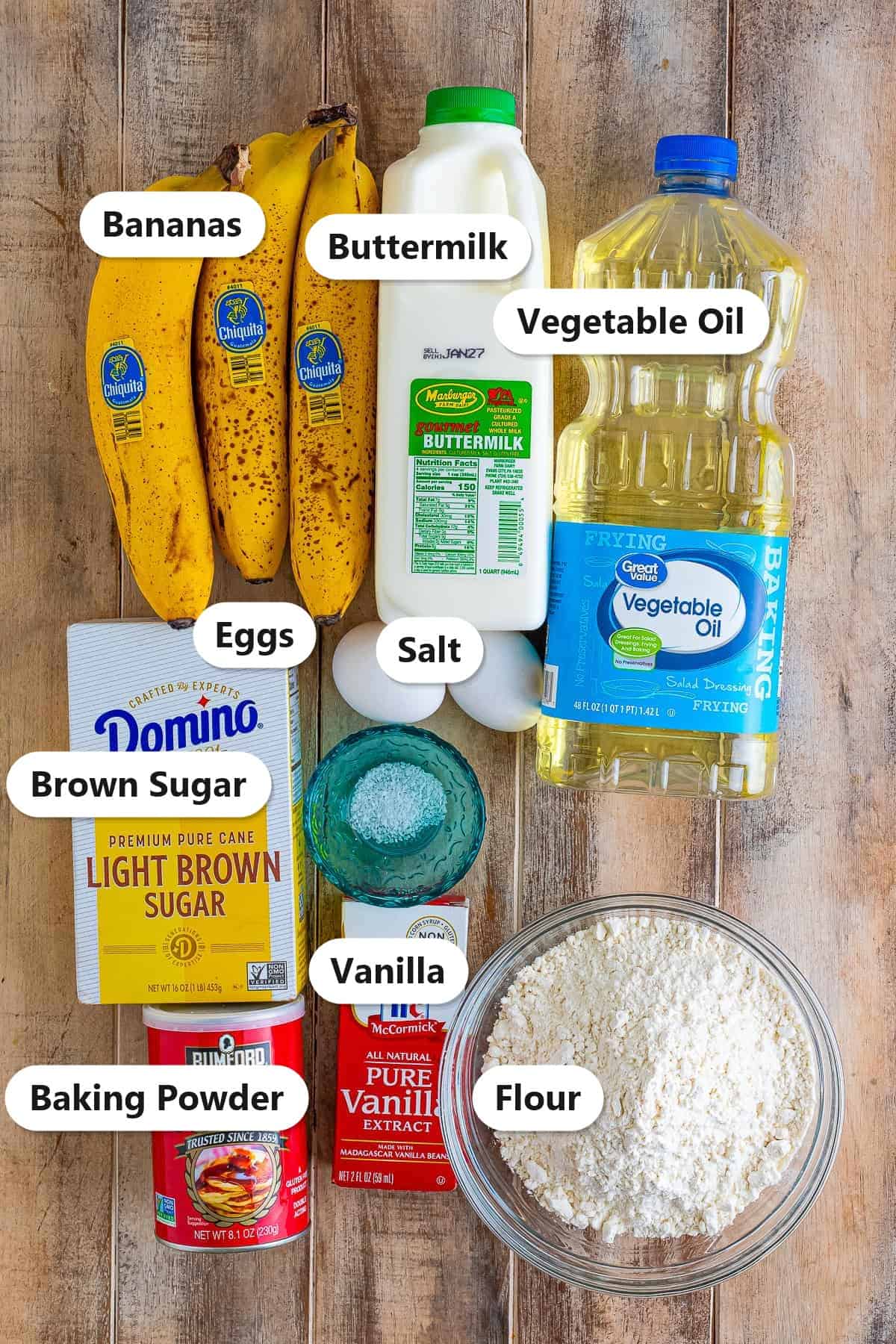 Labeled ingredients for banana fritters including bananas, buttermilk, eggs, brown sugar, oil, vanilla, flour, baking powder, and salt.