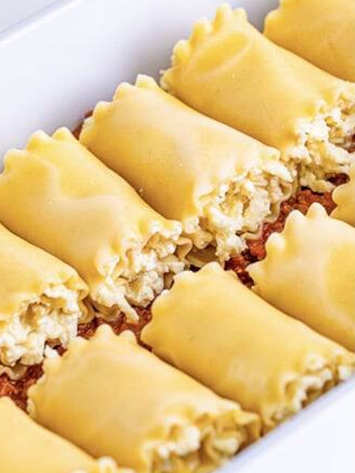 Lasagna noodles spread with ricotta filling and rolled into pinwheels in a sauced baking dish.