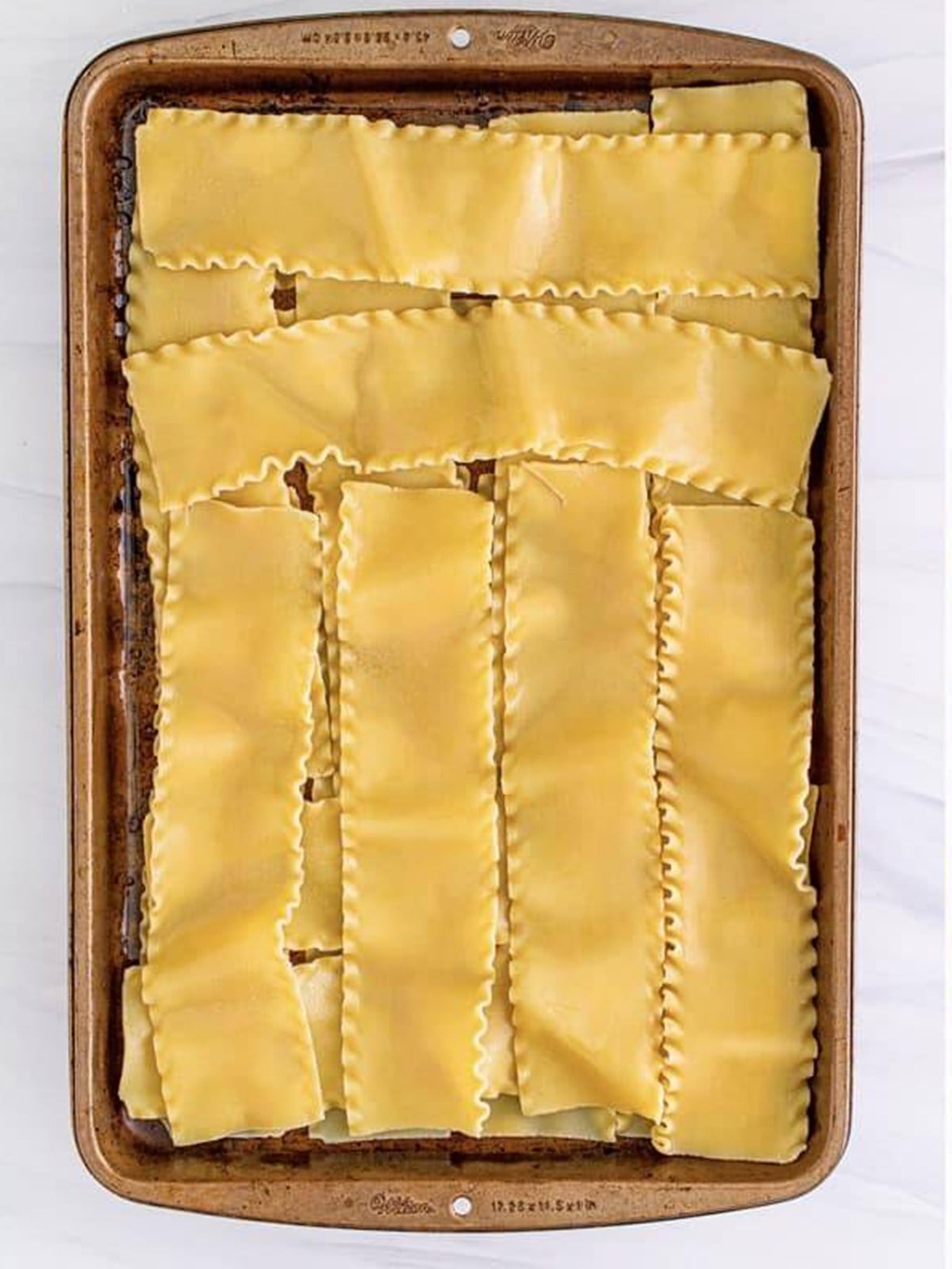 Boiled lasagna noodles laid flat on a greased sheet tray.