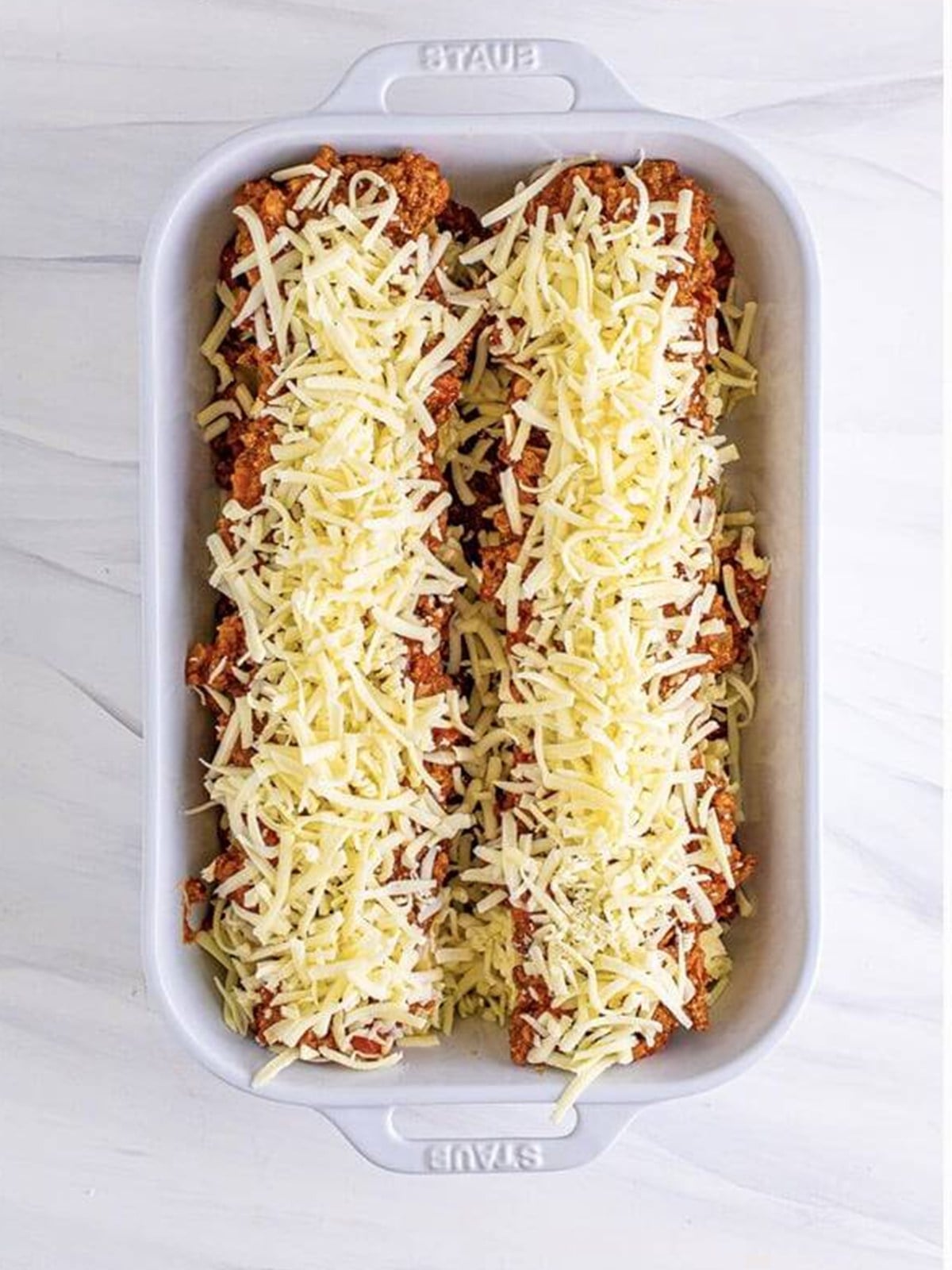 Lasagna roll-ups arranged seam side down in a sauced baking dish.