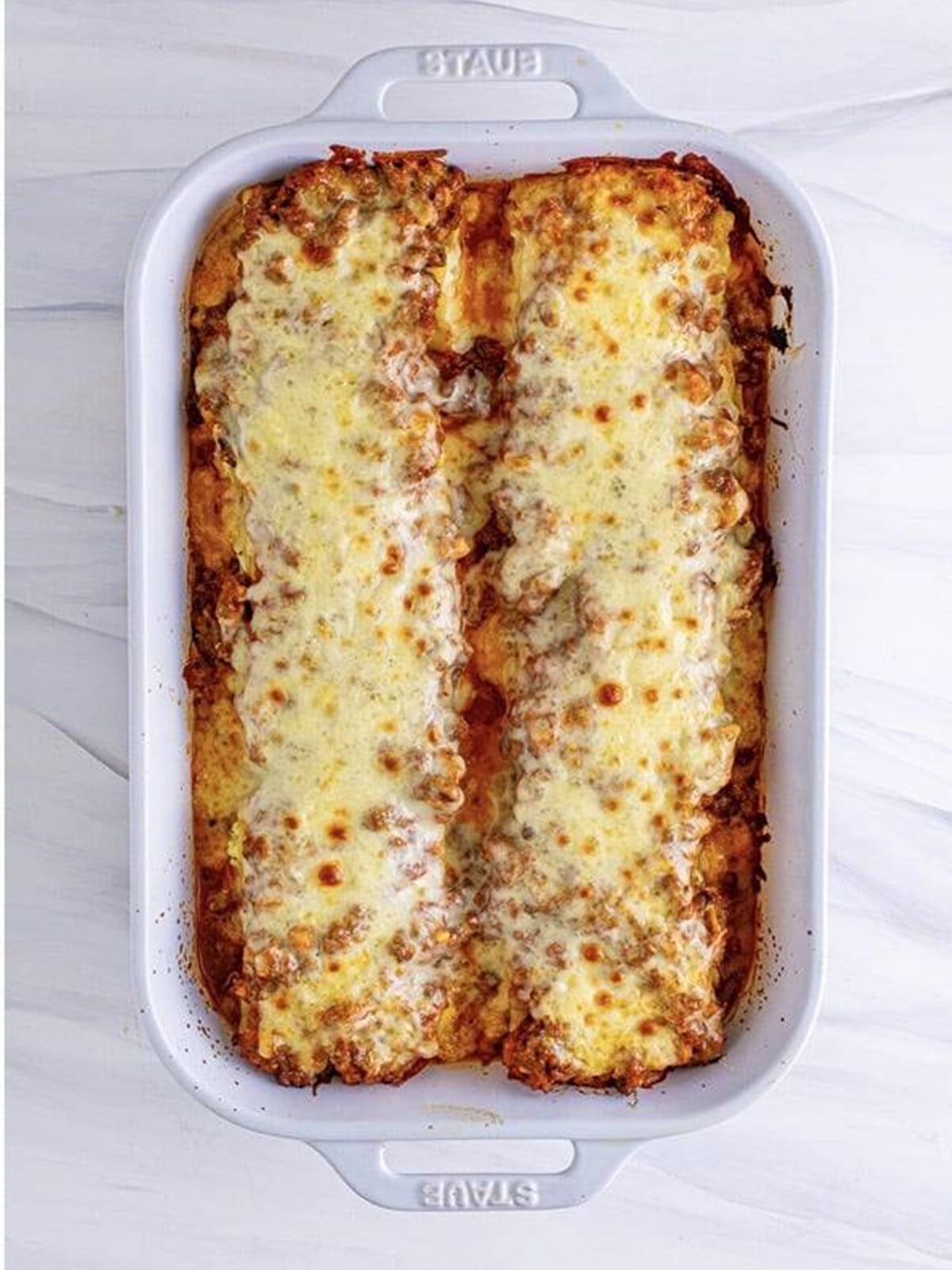 Lasagna roll-ups topped with mozzarella and parmesan before baking.