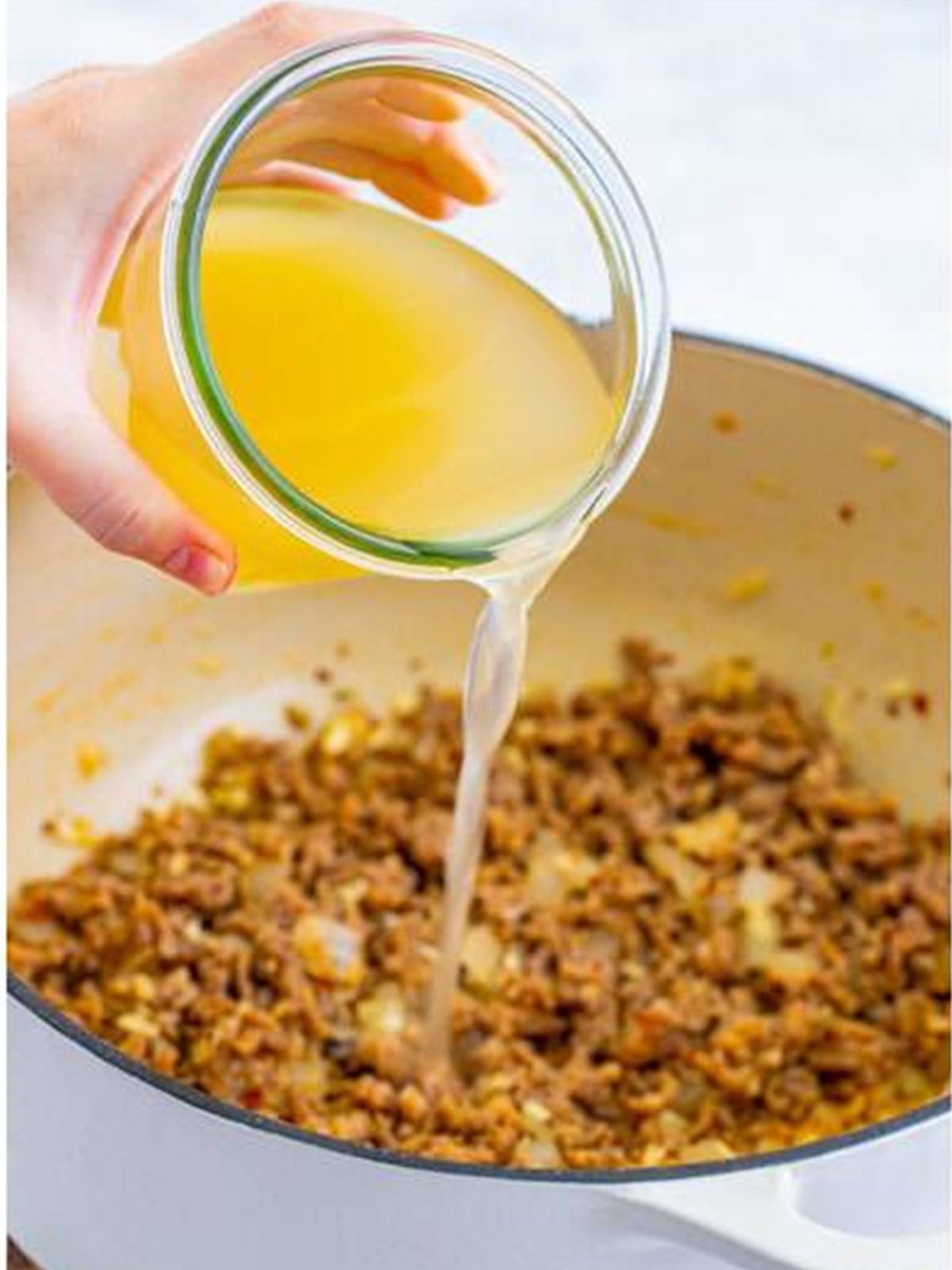 Pouring chicken stock into browned Italian sausage for Lasagna Soup.