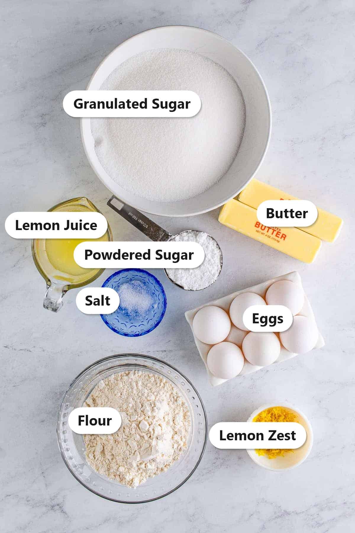 Labeled ingredients for lemon bars including granulated sugar, butter, lemon juice, powdered sugar, salt, eggs, flour, and lemon zest.