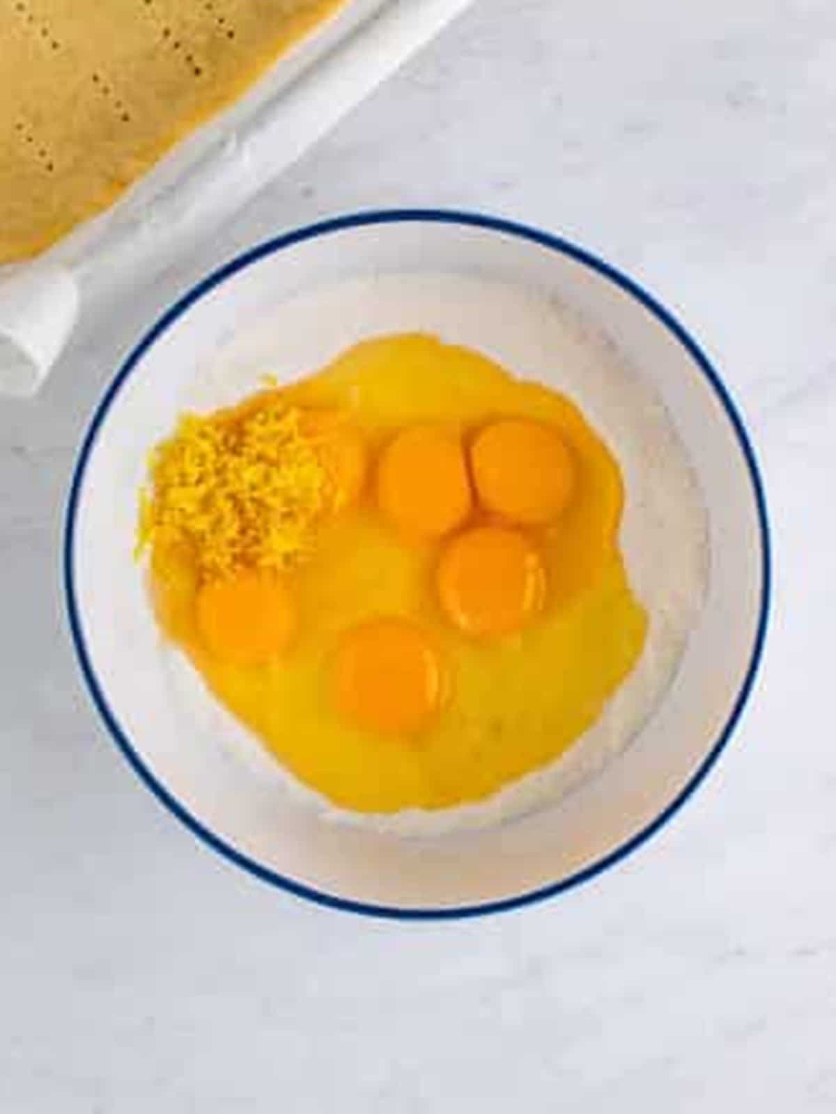 Eggs, lemon zest, sugar, and flour combined in a bowl for lemon bar filling.