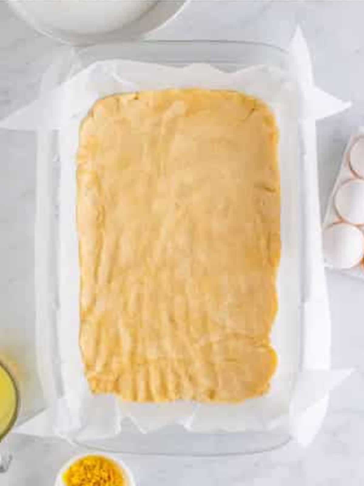 Shortbread crust pressed into a parchment lined baking dish for lemon bars.