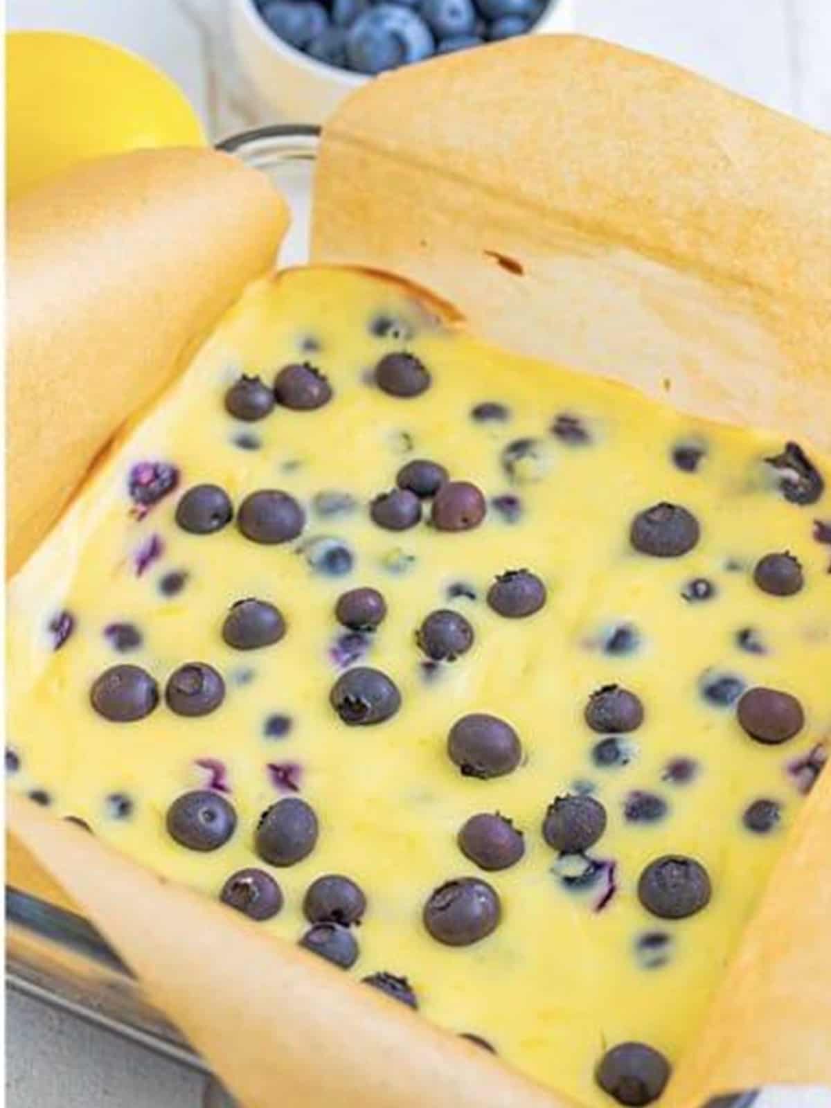 Baked lemon blueberry cheesecake bars in the pan, set with golden edges and studded with blueberries.