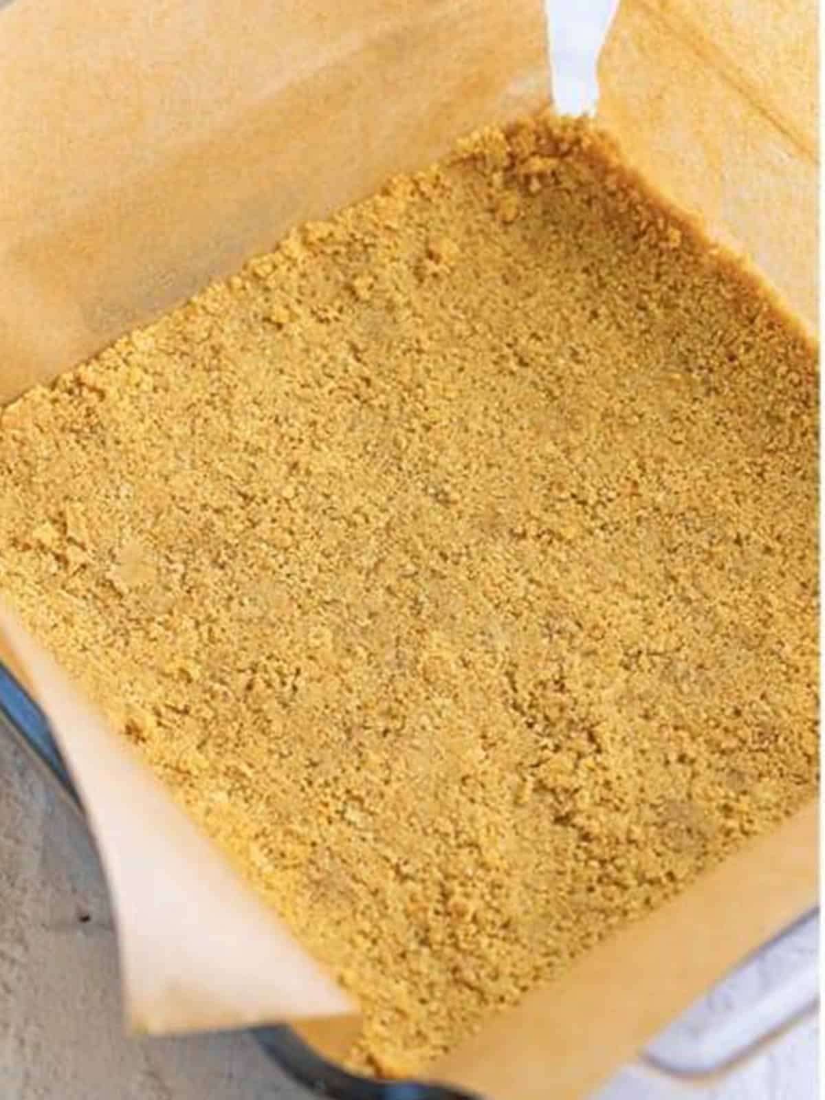 Crushed Golden Oreo crust pressed into the bottom of a parchment-lined baking pan for lemon blueberry cheesecake bars.