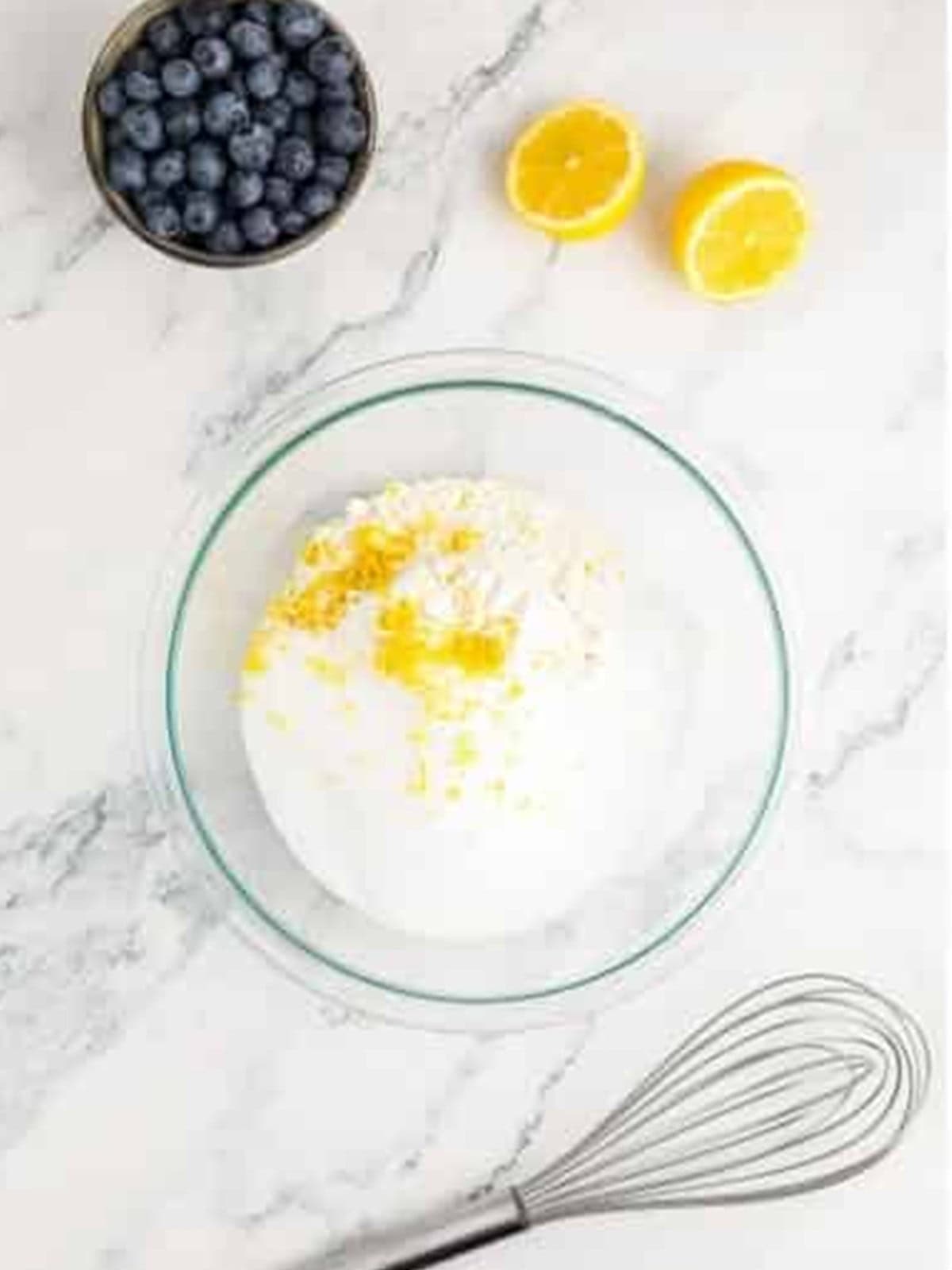 Whisking flour, sugar, baking powder, and lemon zest together in a glass bowl.