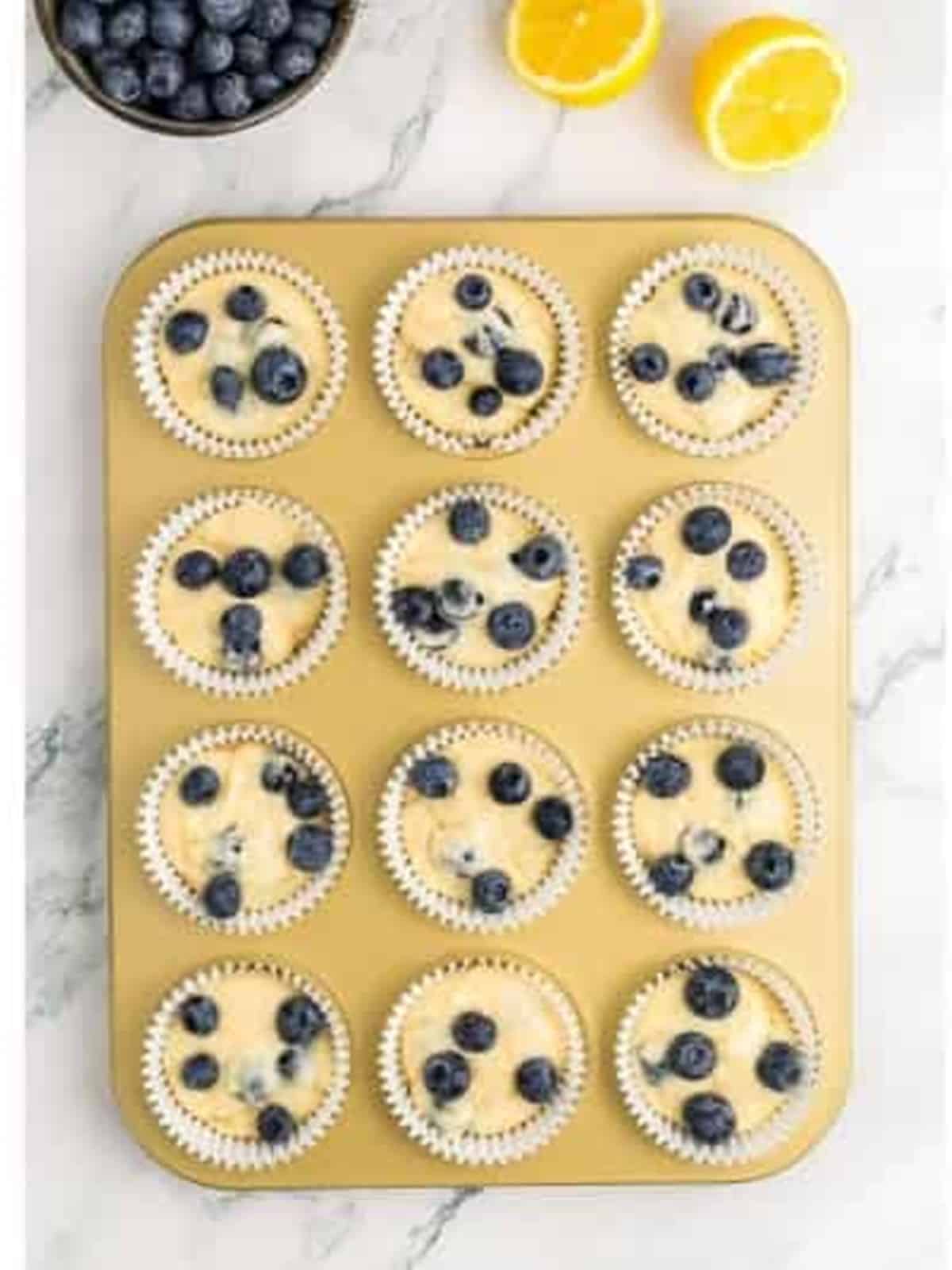Lemon blueberry muffin batter divided into a lined muffin tin and topped with berries.