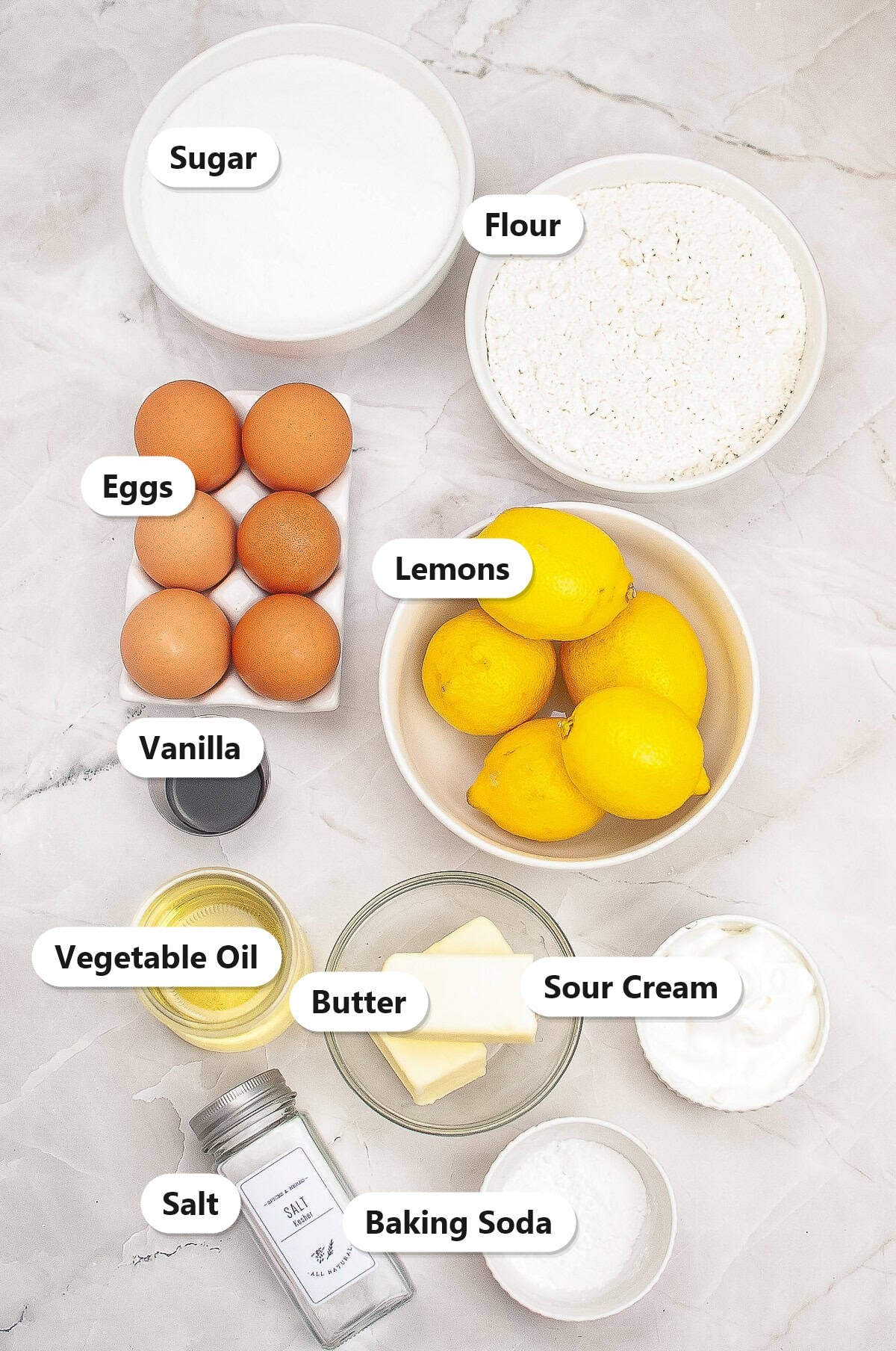 Labeled ingredients for lemon bundt cake including flour, sugar, eggs, lemons, butter, sour cream, and oil.