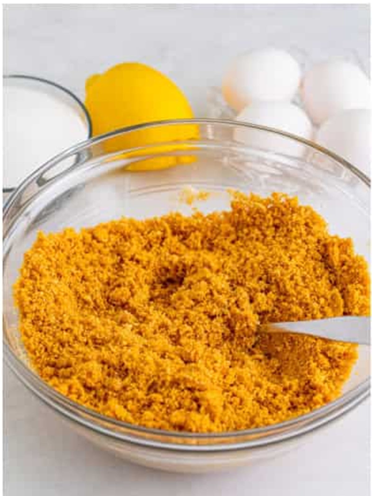 Graham cracker crumbs, sugar, and melted butter mixed in a bowl for the Lemon Cheesecake crust.