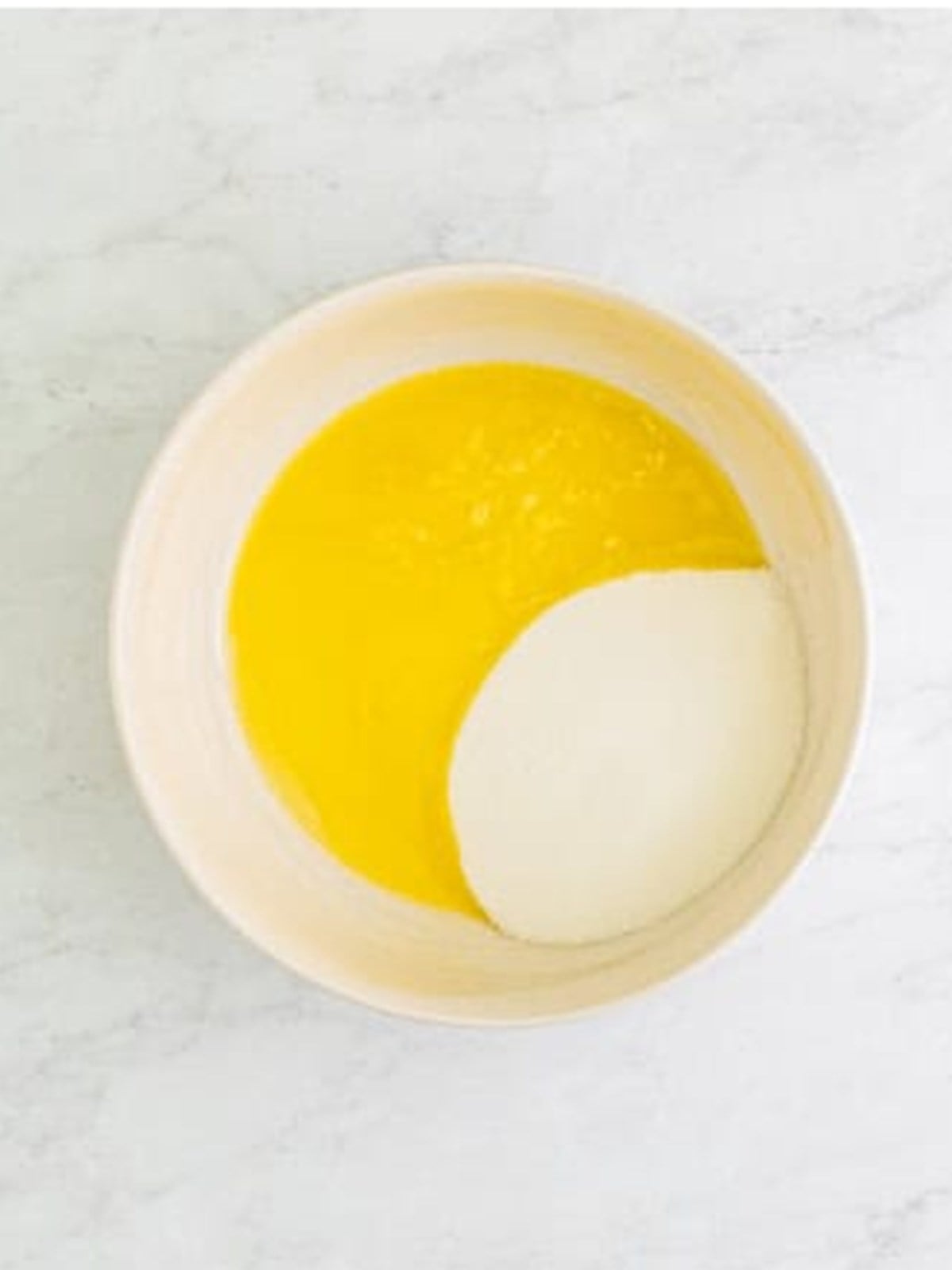 Whisking melted butter, oil, and sugar in a bowl for lemon cupcake batter.
