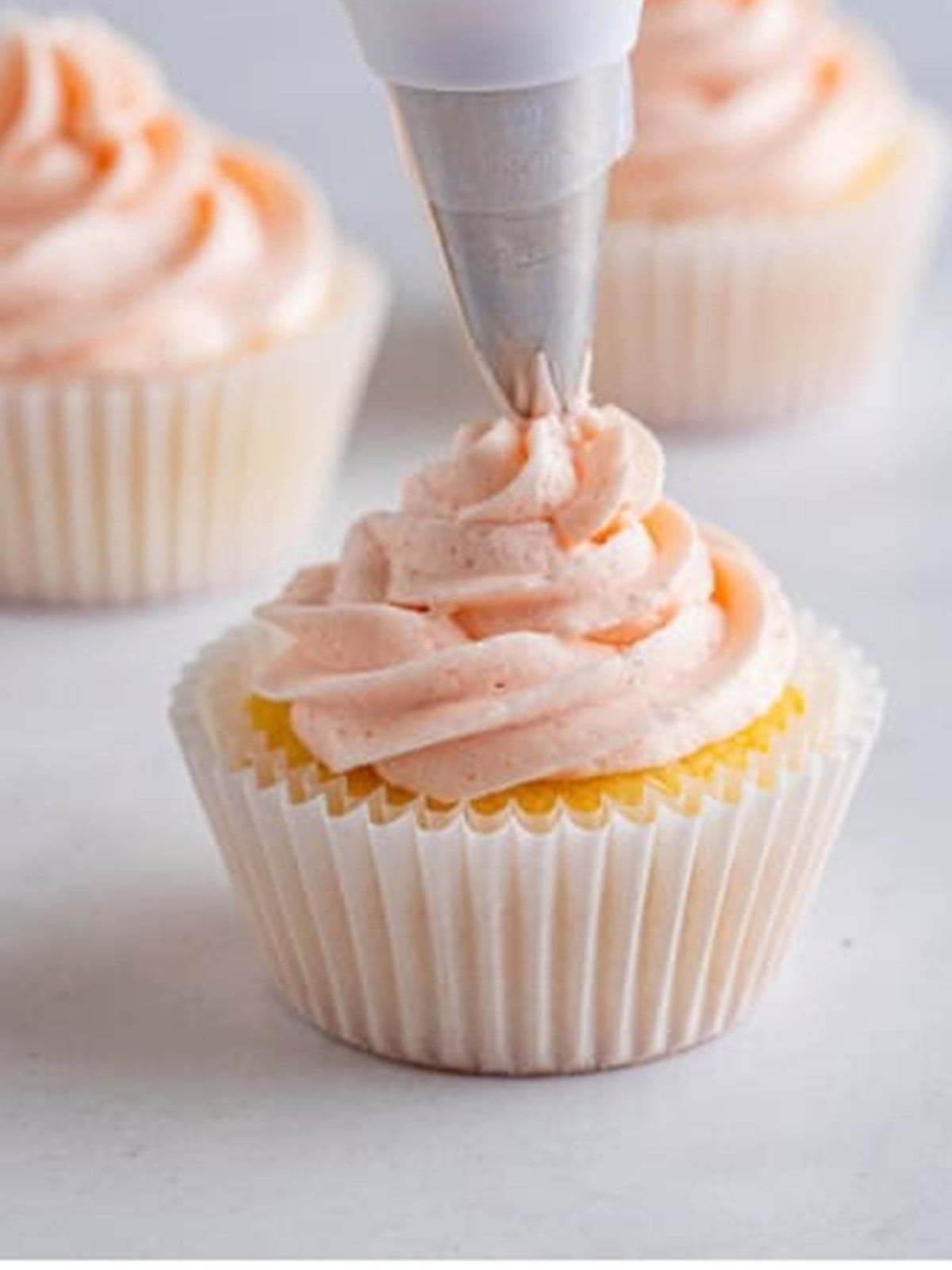 Piping strawberry buttercream onto a lemon cupcake.