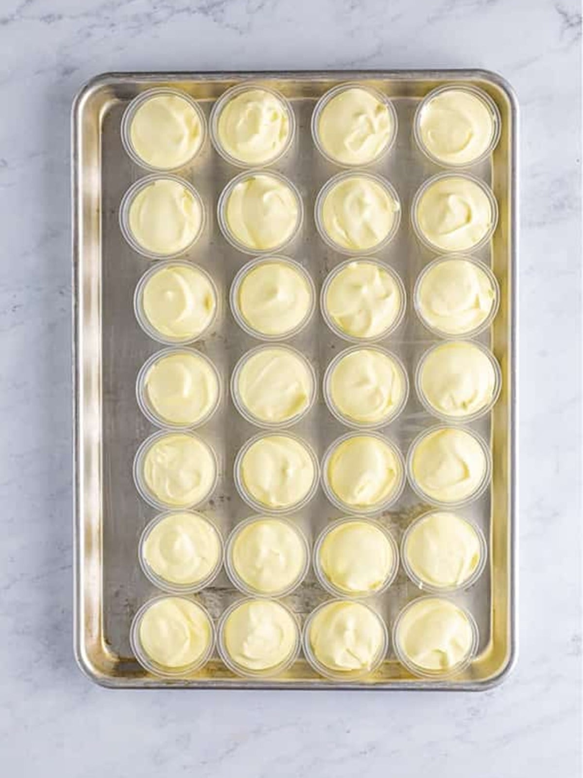 Two ounce plastic shot cups filled with limoncello lemon pudding on a sheet tray.