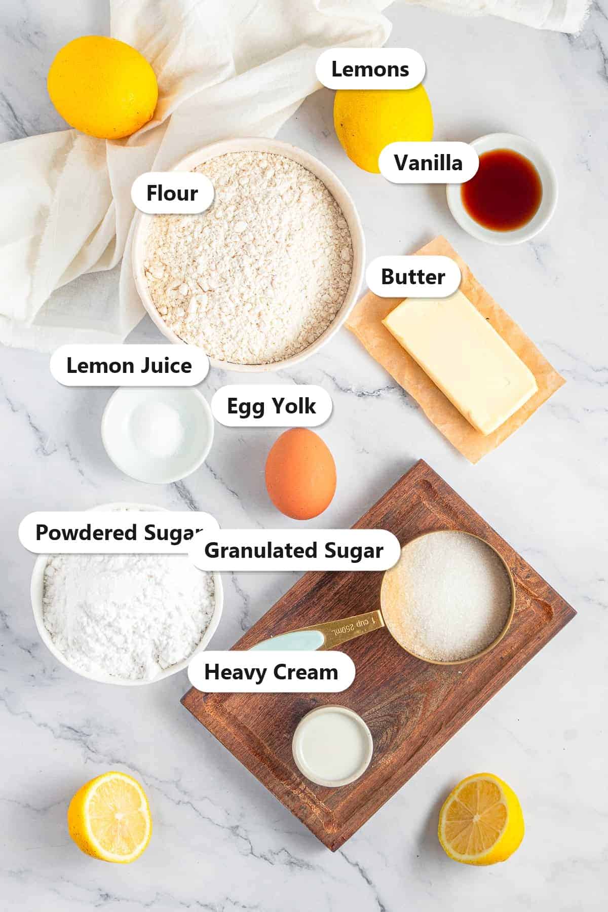 Labeled ingredients for lemon sandwich cookies including butter, granulated sugar, lemon juice, lemon zest, vanilla, egg yolk, flour, powdered sugar, and heavy cream.