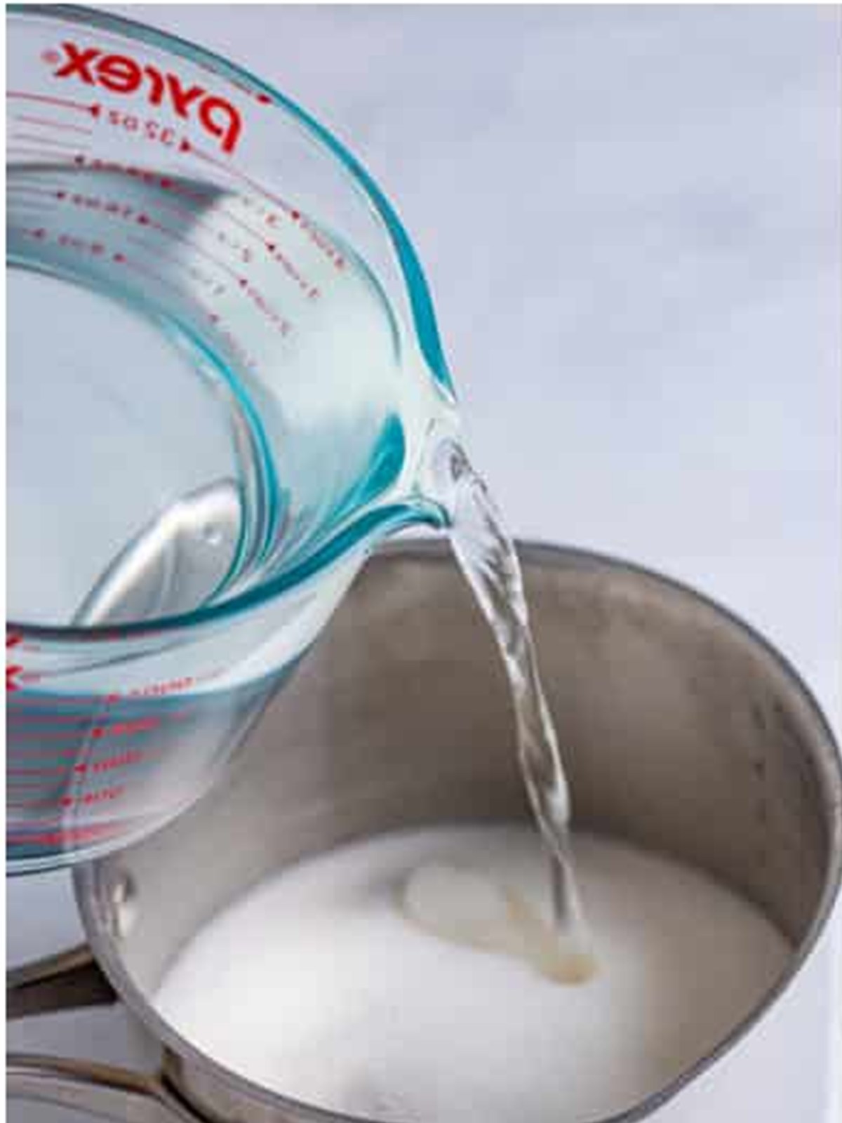 Pouring water into a saucepan with granulated sugar to dissolve it into simple syrup for lemonade.