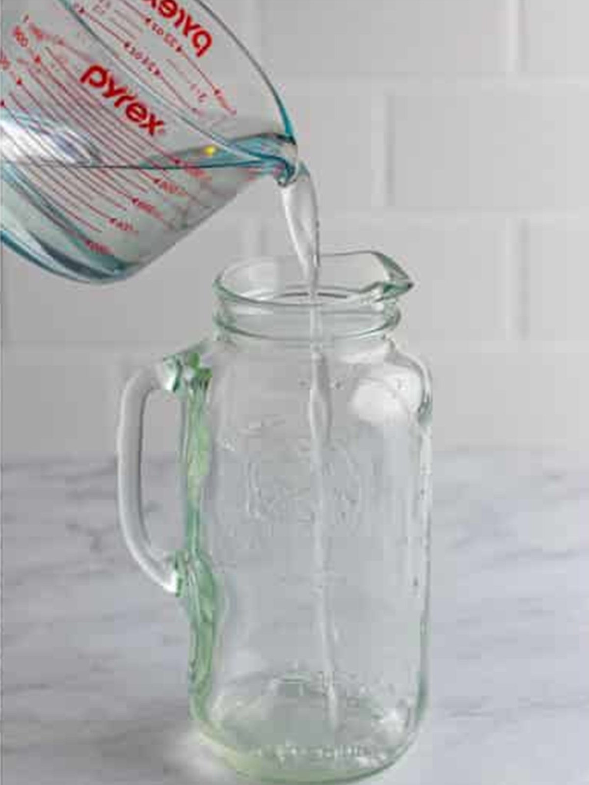 Pouring cold water into a large glass pitcher for homemade lemonade.
