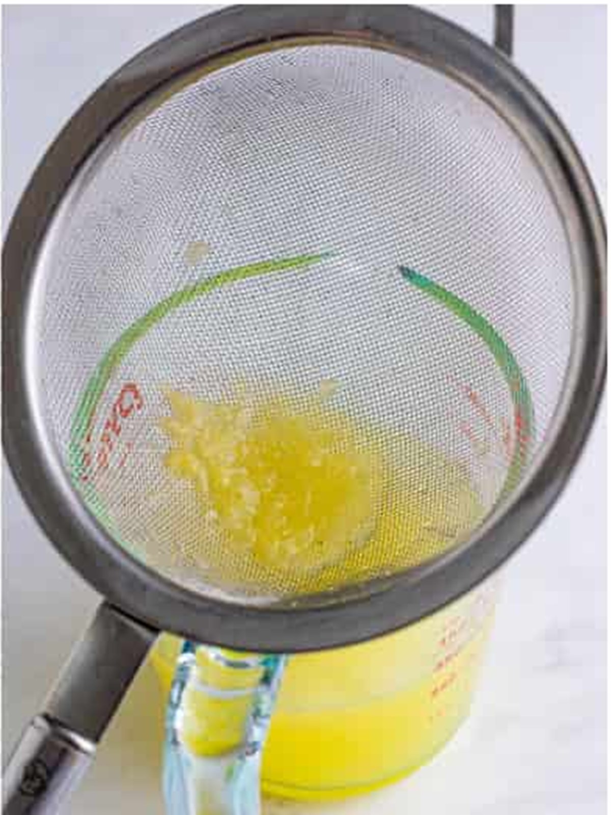 Straining fresh lemon juice through a fine mesh strainer for lemonade.