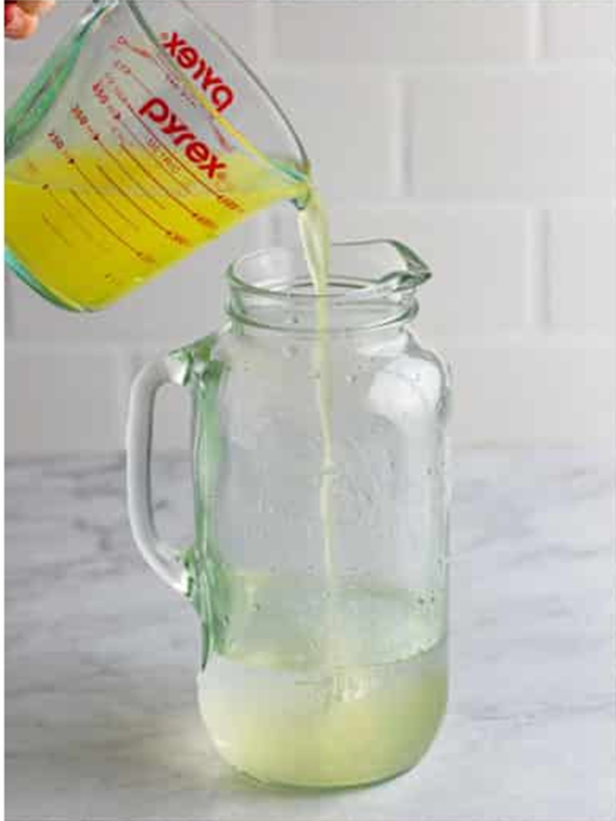 Adding fresh strained lemon juice into the pitcher to make lemonade.