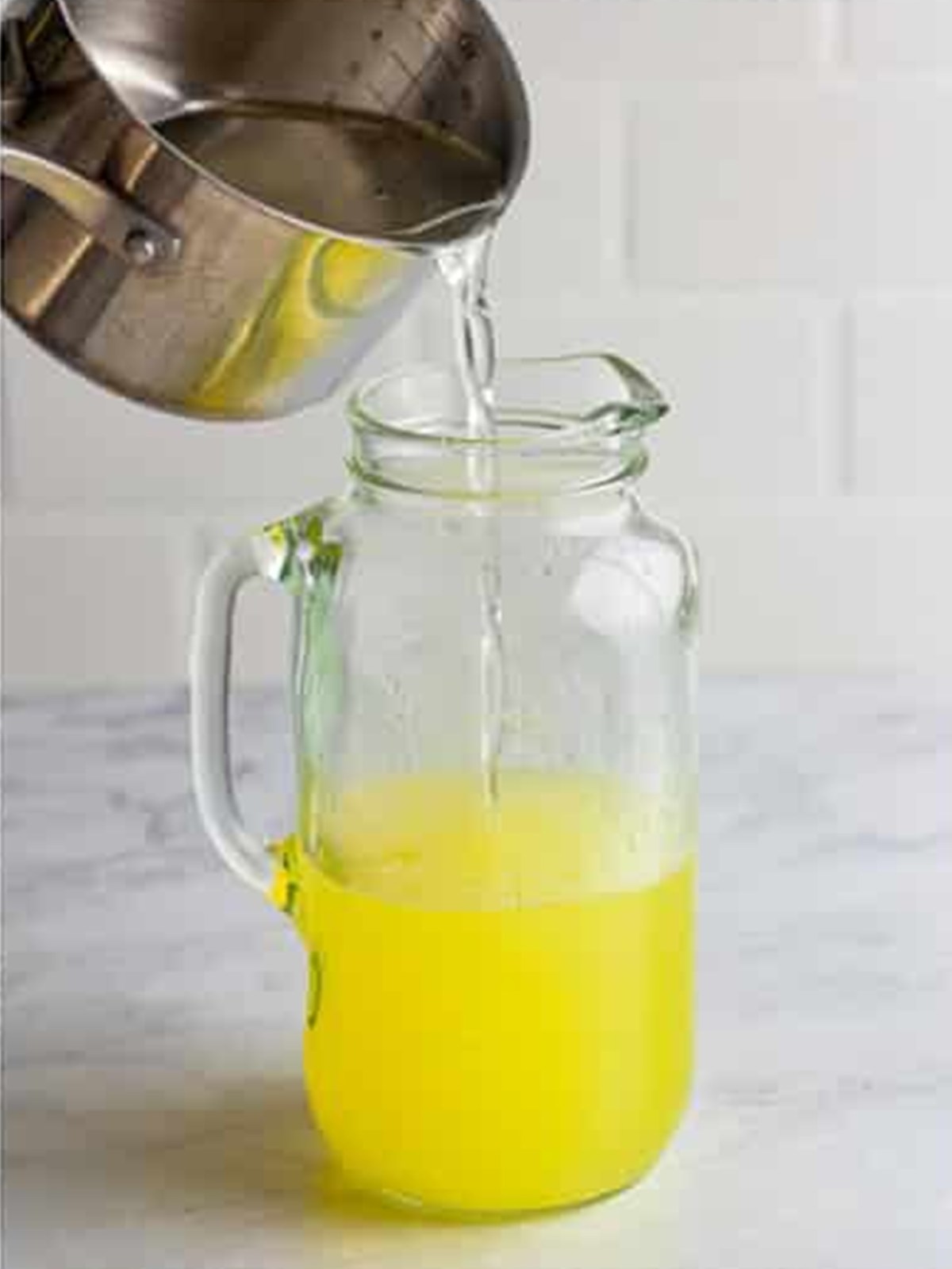 Pouring cooled sugar simple syrup into the pitcher of water and lemon juice.