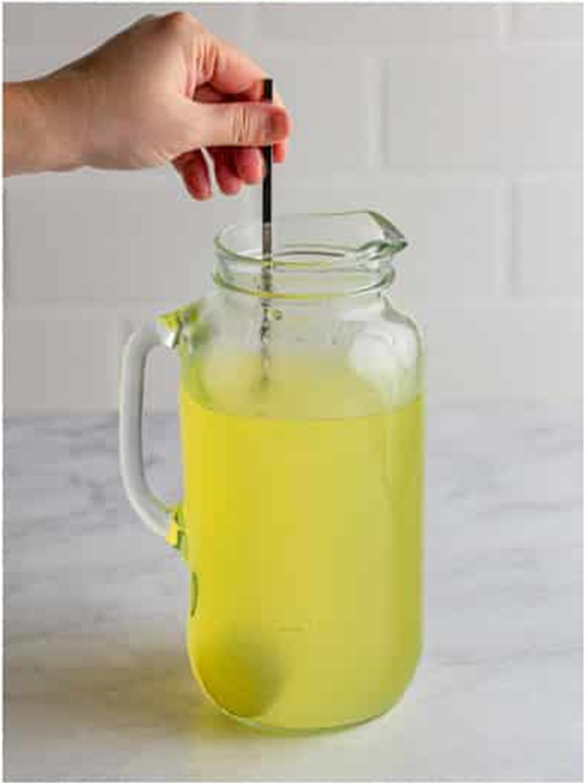 Stirring homemade lemonade in a glass pitcher before chilling over ice.