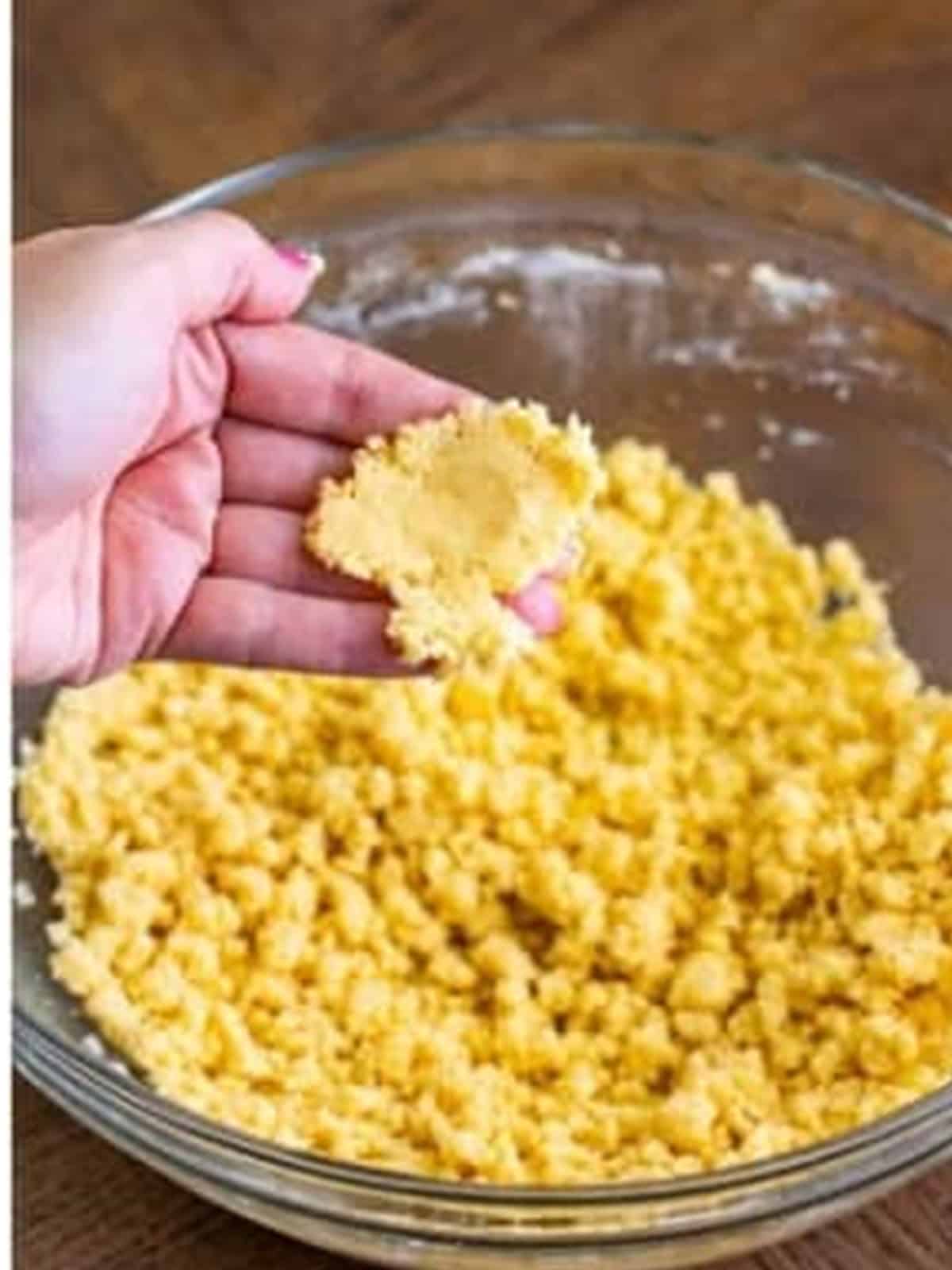 Crumbly shortbread tart crust dough for lemonade tart pressed in a hand.