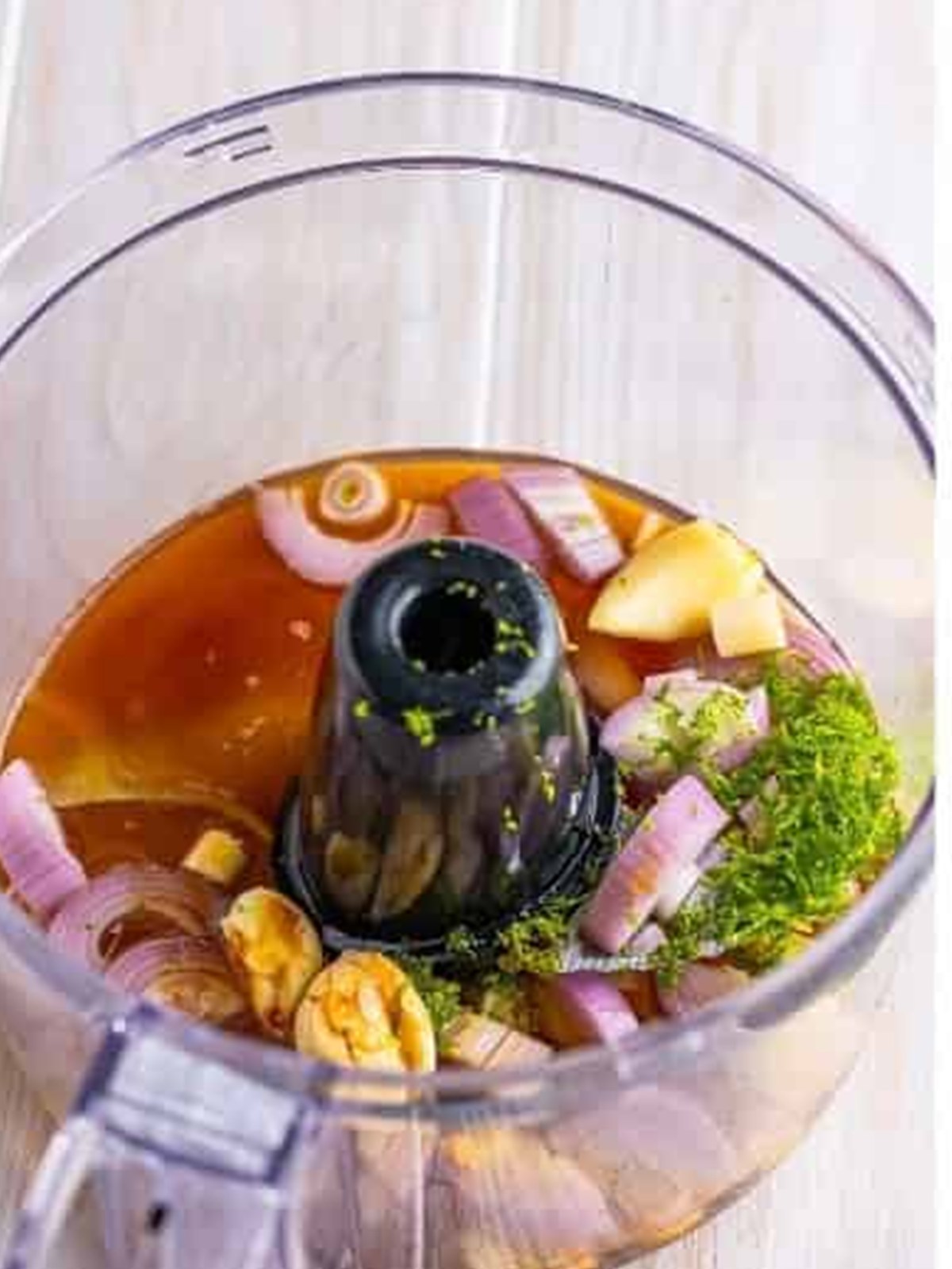 Adding lemongrass, garlic, lime, and sauces to a food processor for lemongrass chicken marinade.