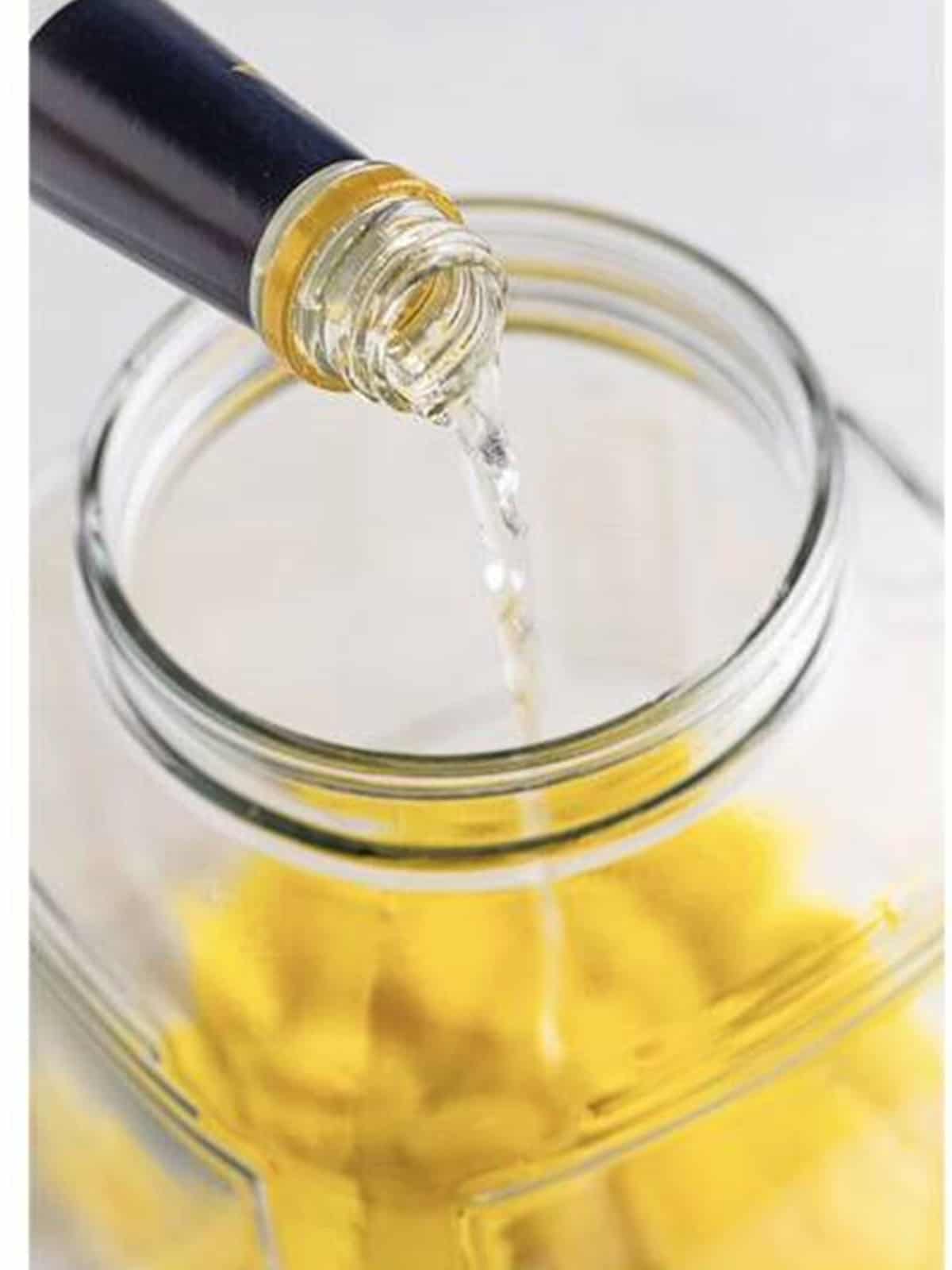 Pouring Everclear over lemon peels in a glass jar for limoncello recipe.
