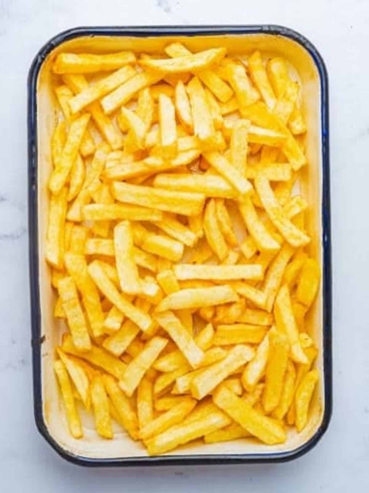 Crispy golden french fries arranged in a baking dish for loaded fries.