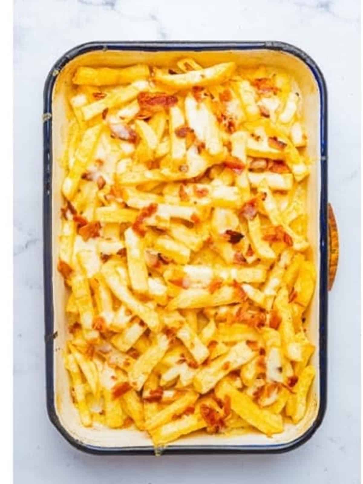 Shredded cheese and chopped bacon sprinkled over french fries in a baking dish.