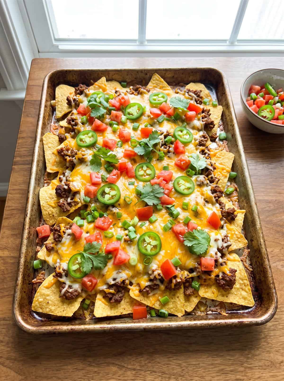 Baked loaded nachos topped with tomato, jalapeno, green onion, and cilantro.