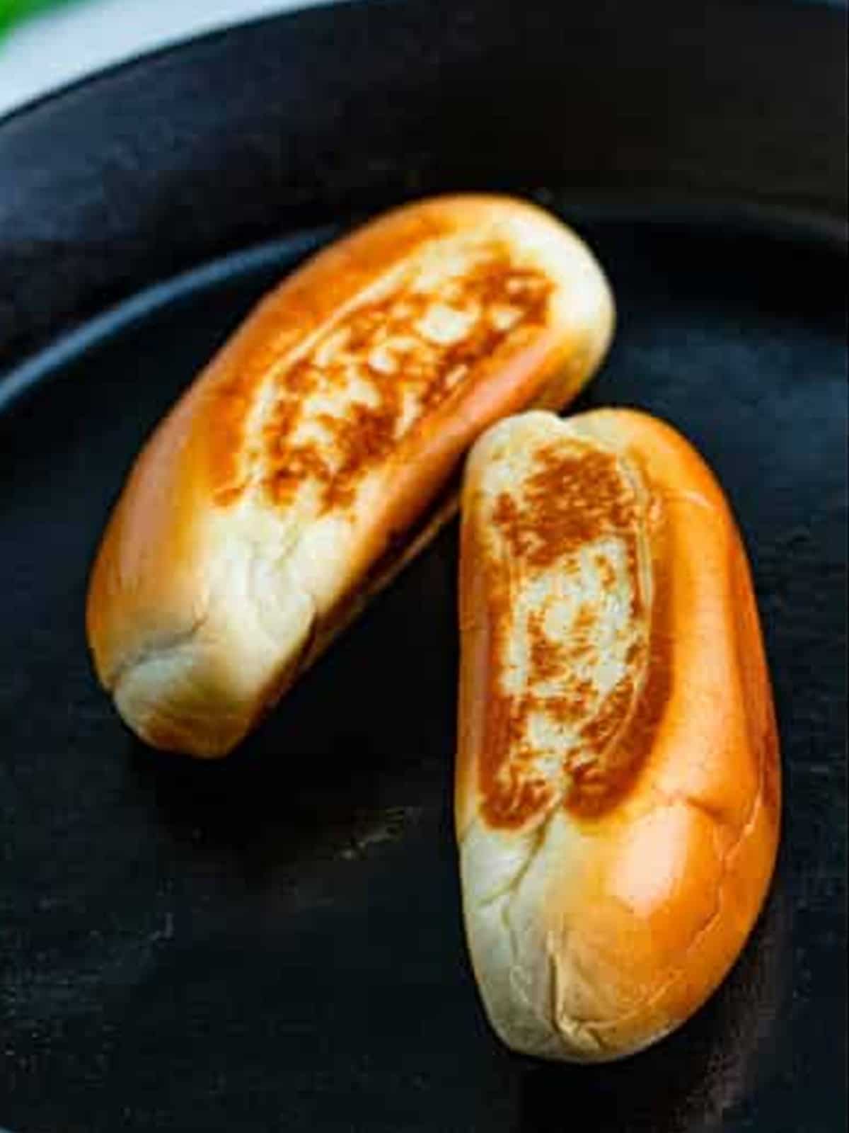 Buttered hot dog buns toasted golden in a cast iron skillet.