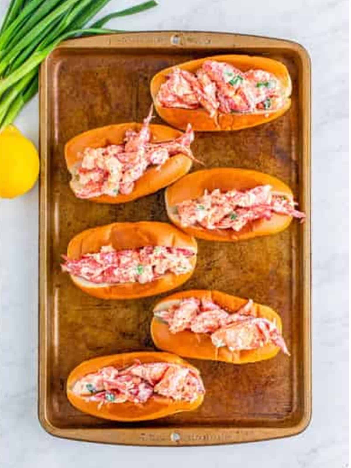 Toasted buns filled with the lobster mixture on a sheet tray.