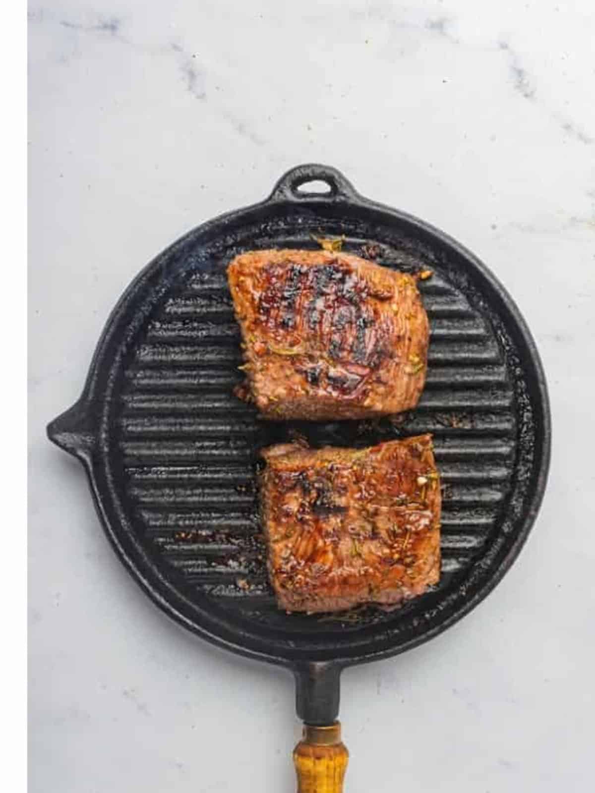 Seared London broil resting on the grill pan after cooking to temperature.
