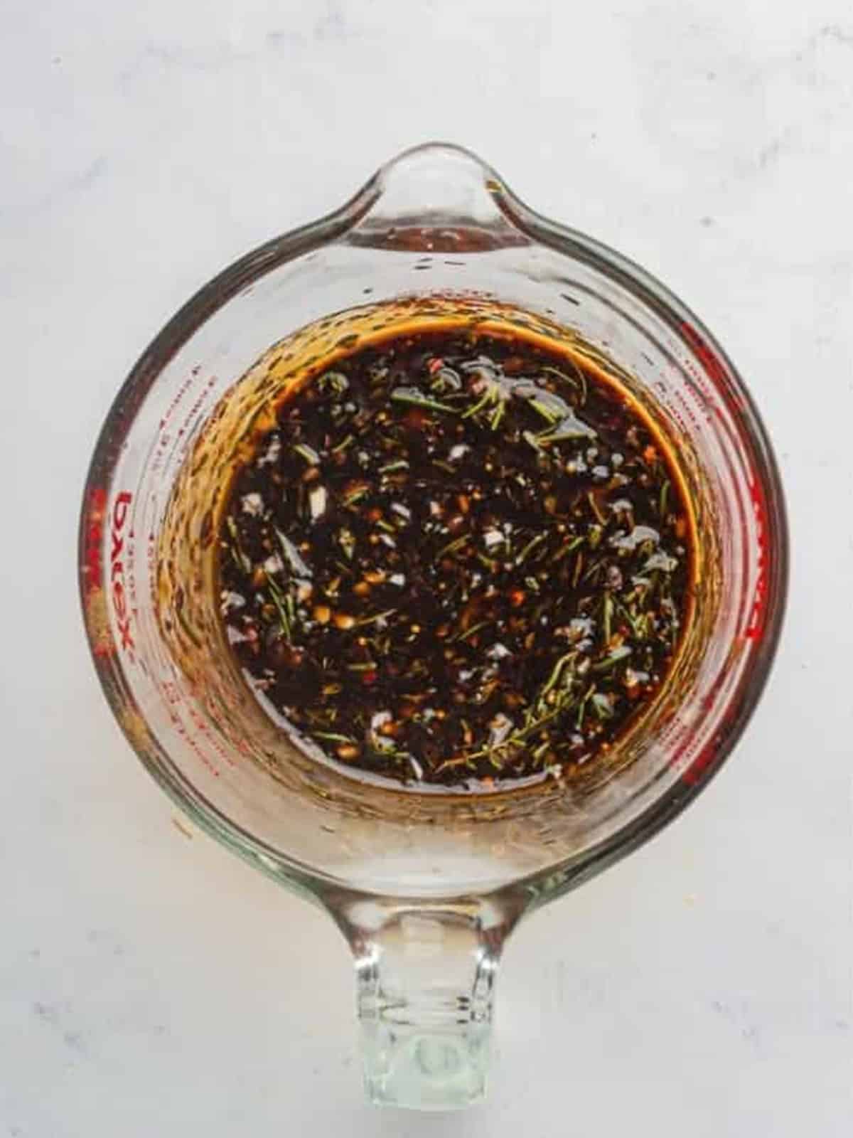 Whisking the London broil marinade with balsamic vinegar, mustard, honey, and fresh herbs in a bowl.